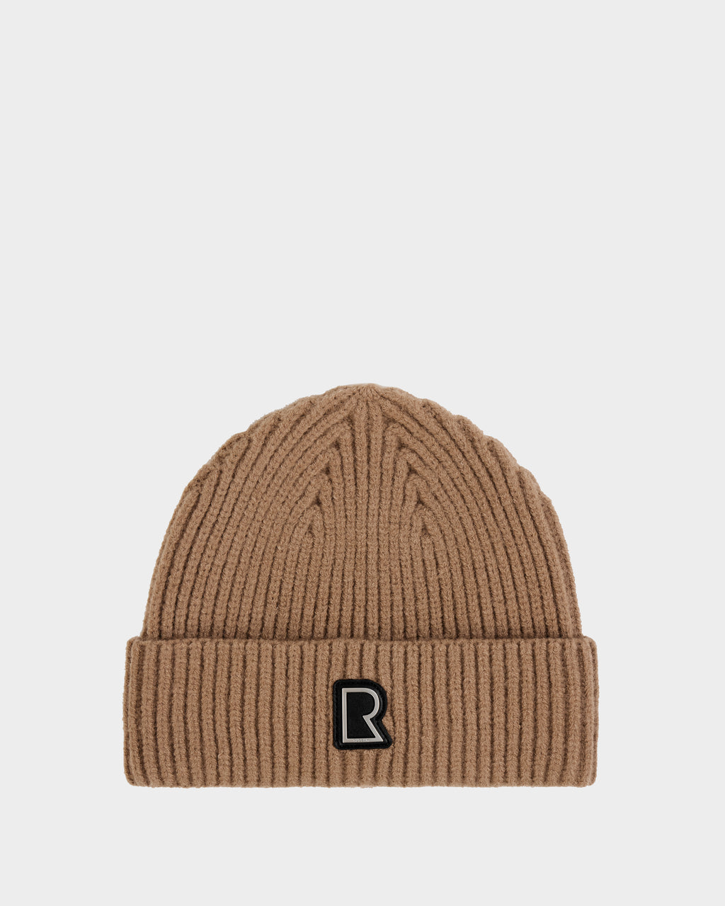 The JULIO - U423502 Sand by Rudsak is a ribbed, light brown unisex knit beanie with a folded brim and a black patch featuring a white outlined R logo on the front. The background is plain white—a true winter essential.