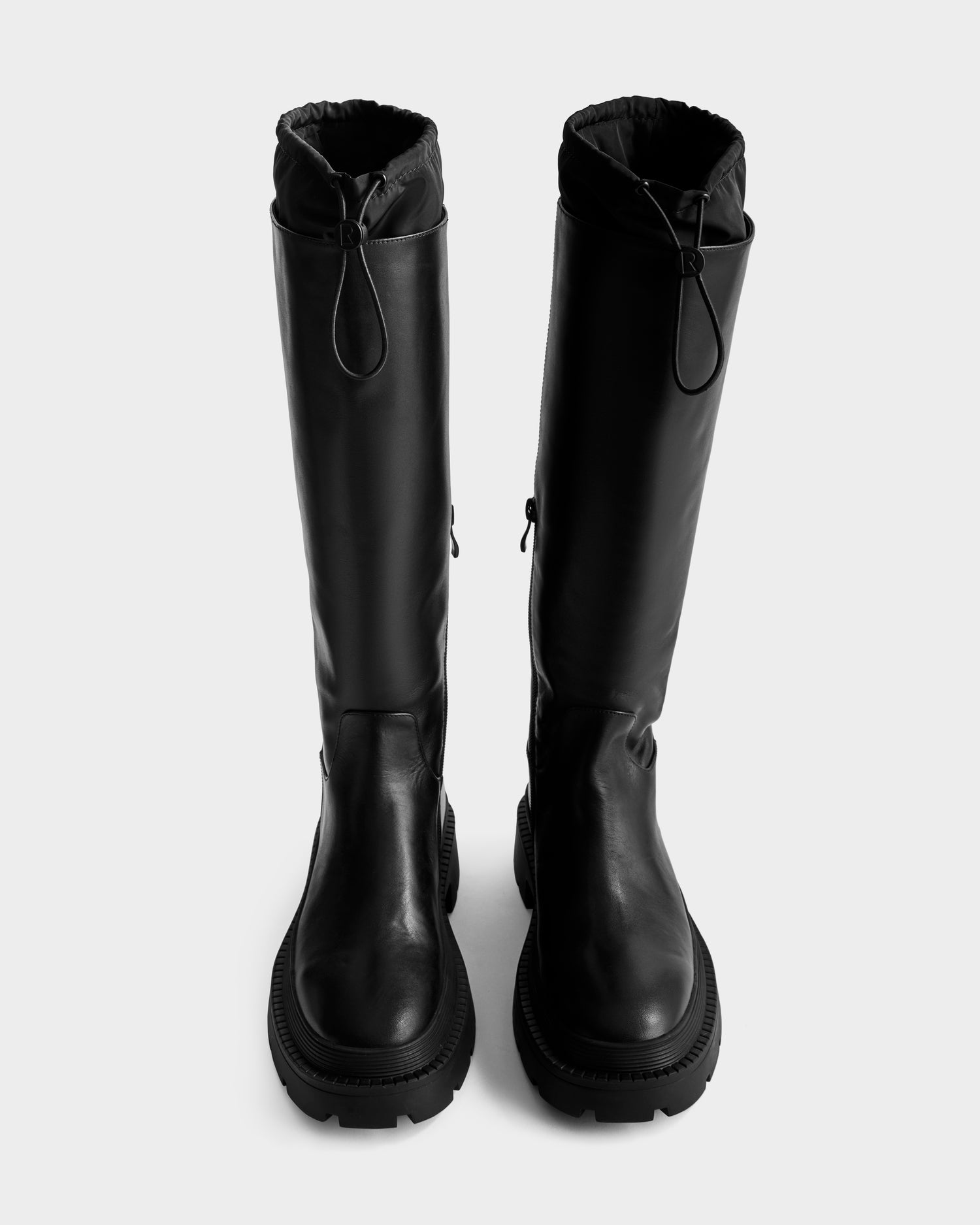 The Rudsak KAROL - 8225576 Black women’s high leather boots feature a tall silhouette, chunky rubber soles, and front drawstring closures, shown upright on a light gray background.