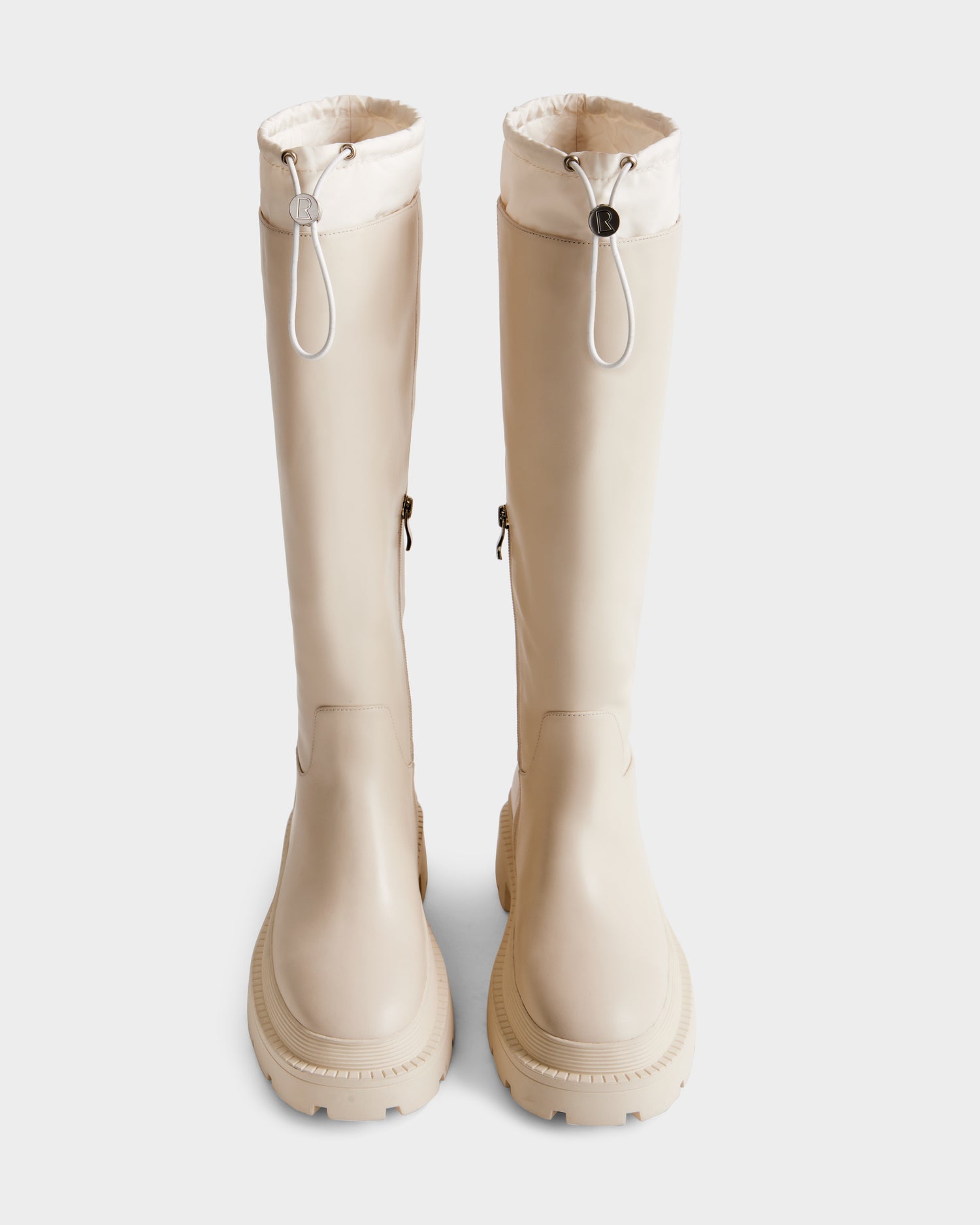 The KAROL - 8225576 Vanilla boots by Rudsak feature a tall beige design with a chunky rubber sole, adjustable cuff with white drawstring closures, and side buckles, shown against a plain white background.