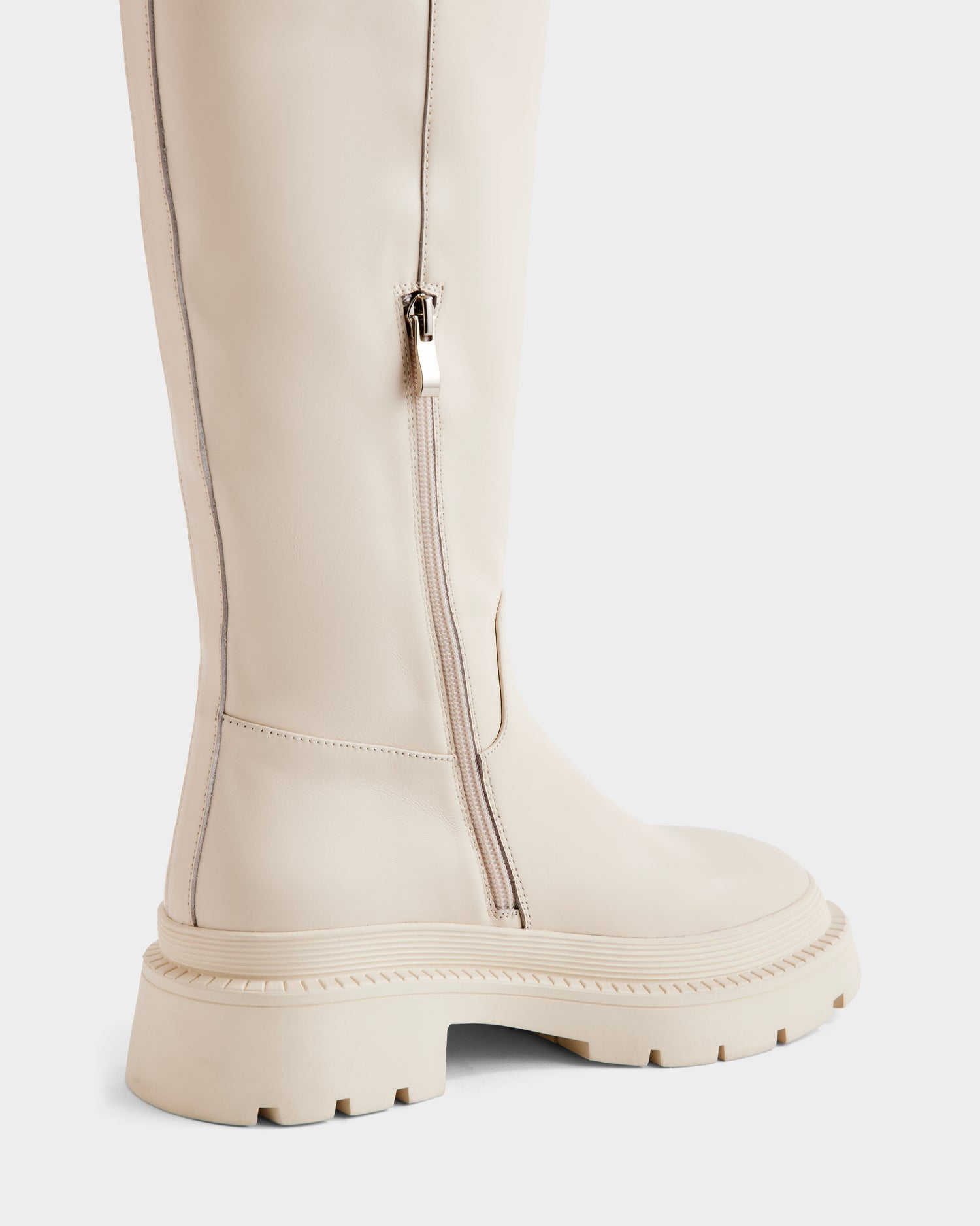 A close-up side view of the Rudsak KAROL - 8225576 Vanilla, a tall off-white women’s leather boot with a chunky rubber sole, adjustable cuff, and zipper along the ankle and calf.