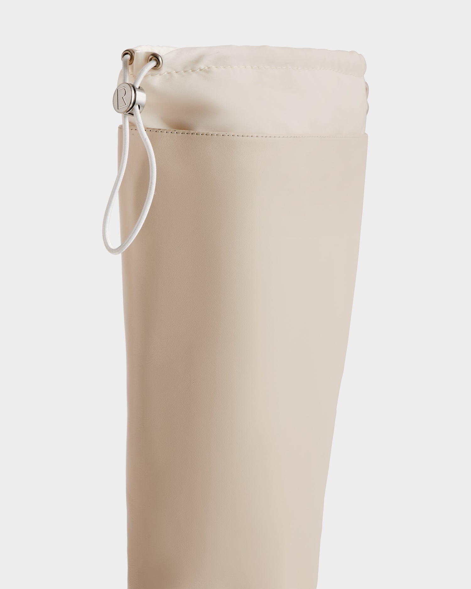 Close-up of the KAROL - 8225576 Vanilla bag by Rudsak, a beige cylindrical pouch with a cinch closure, white cord, and silver button on a white background.