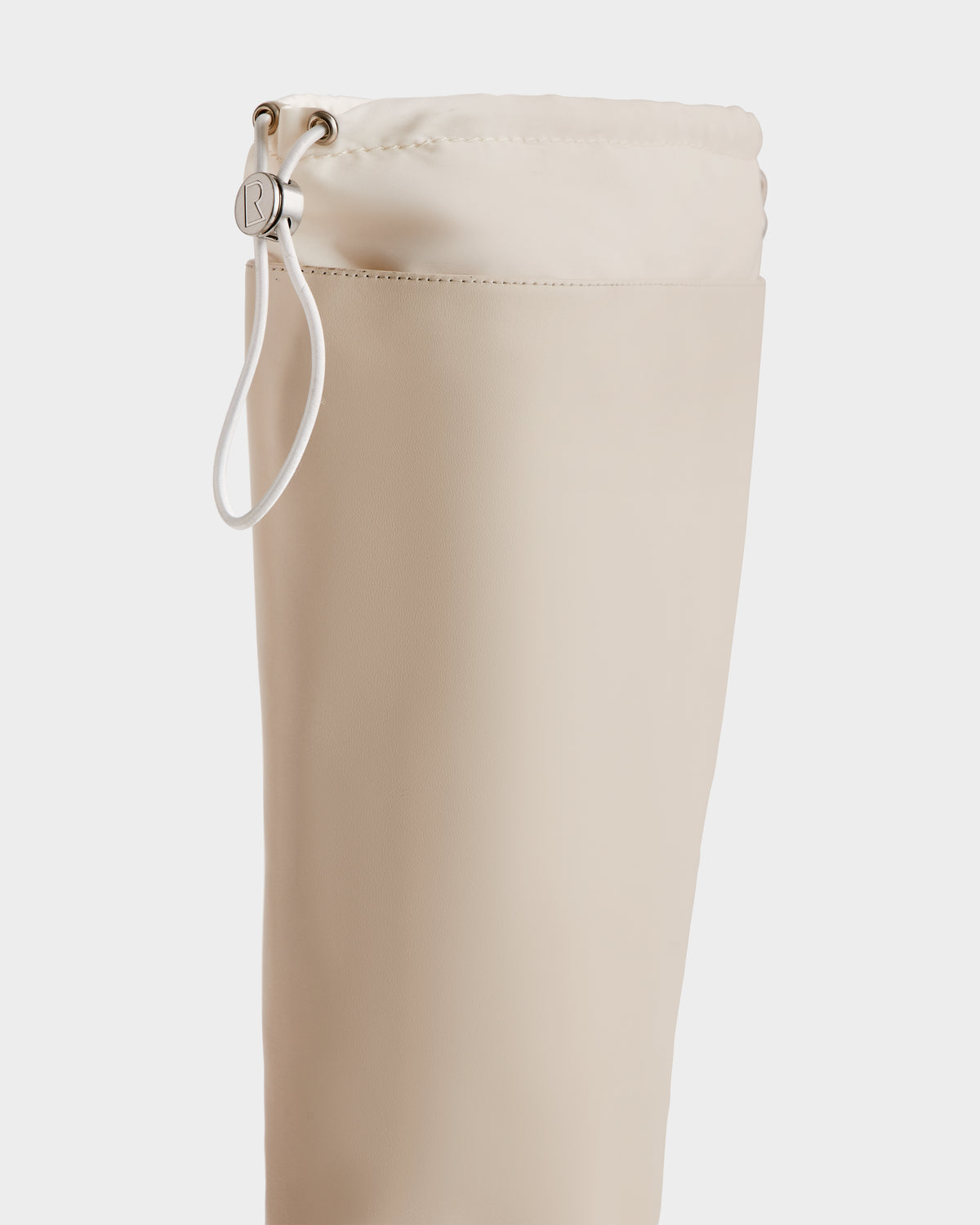 Close-up of the KAROL - 8225576 Vanilla bag by Rudsak, a beige cylindrical pouch with a cinch closure, white cord, and silver button on a white background.