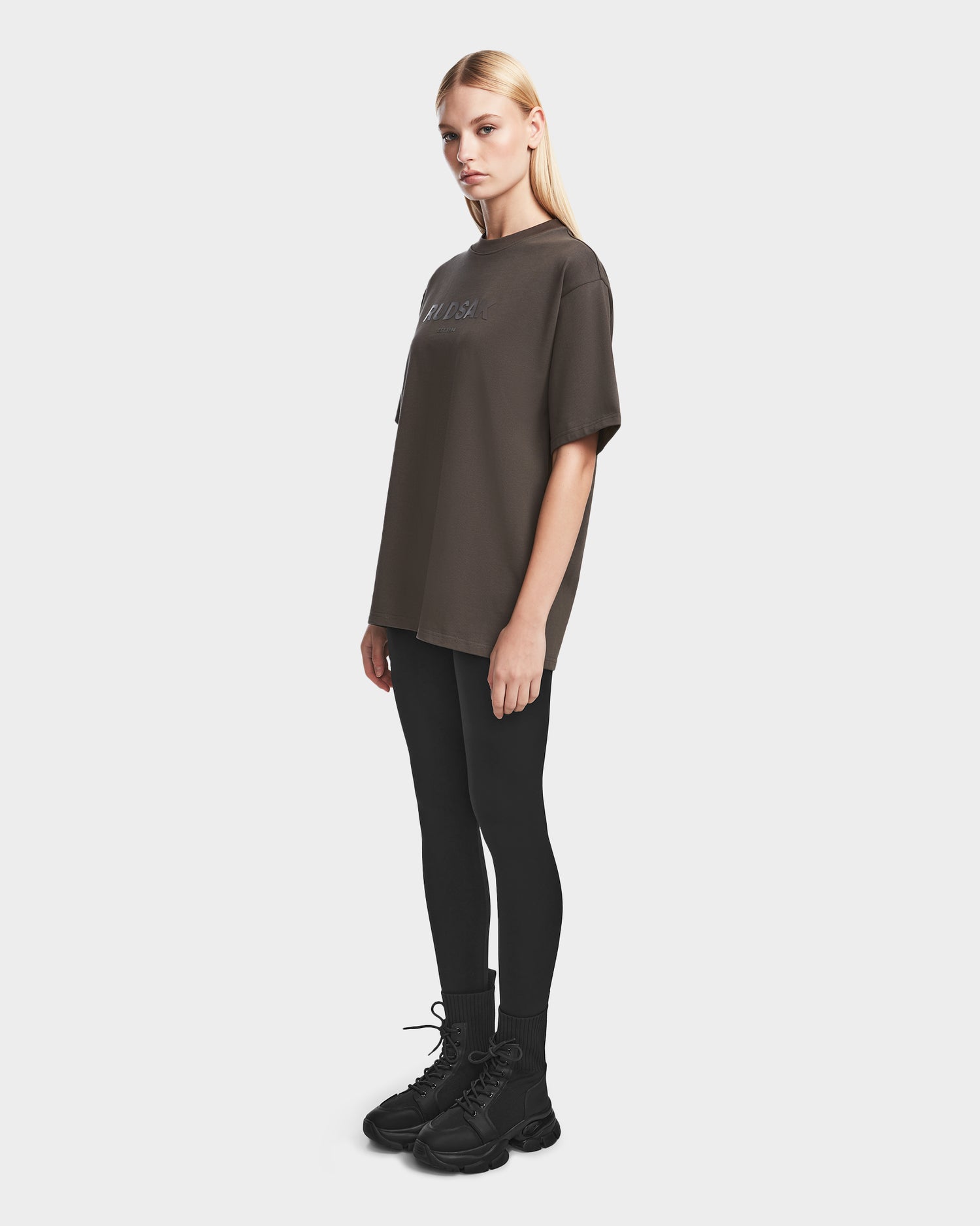 A woman wears the Rudsak KARTER - 9524008 Grey W, an oversized unisex T-shirt crafted from premium cotton, featuring a relaxed fit.