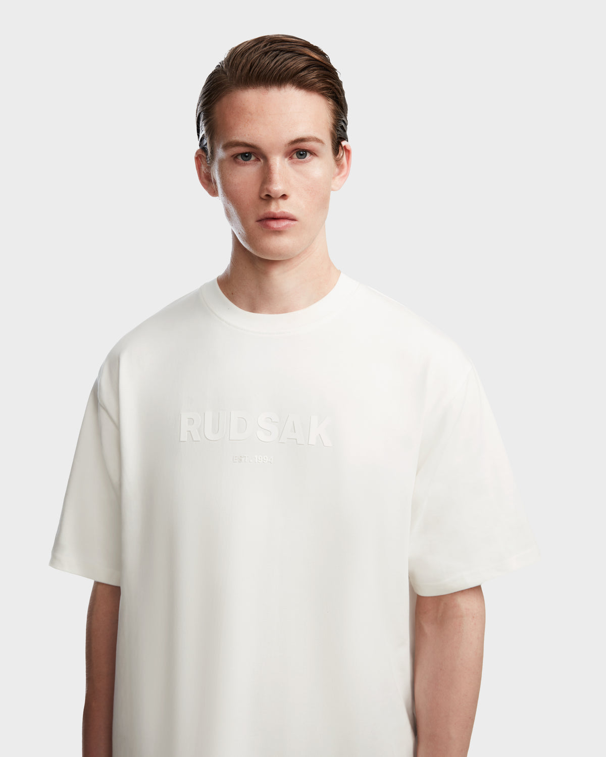 A young person with short brown hair wears the Rudsak KARTER - 9524008 Iceland M premium cotton T-shirt, standing against a plain light gray background and looking directly at the camera with a neutral expression.