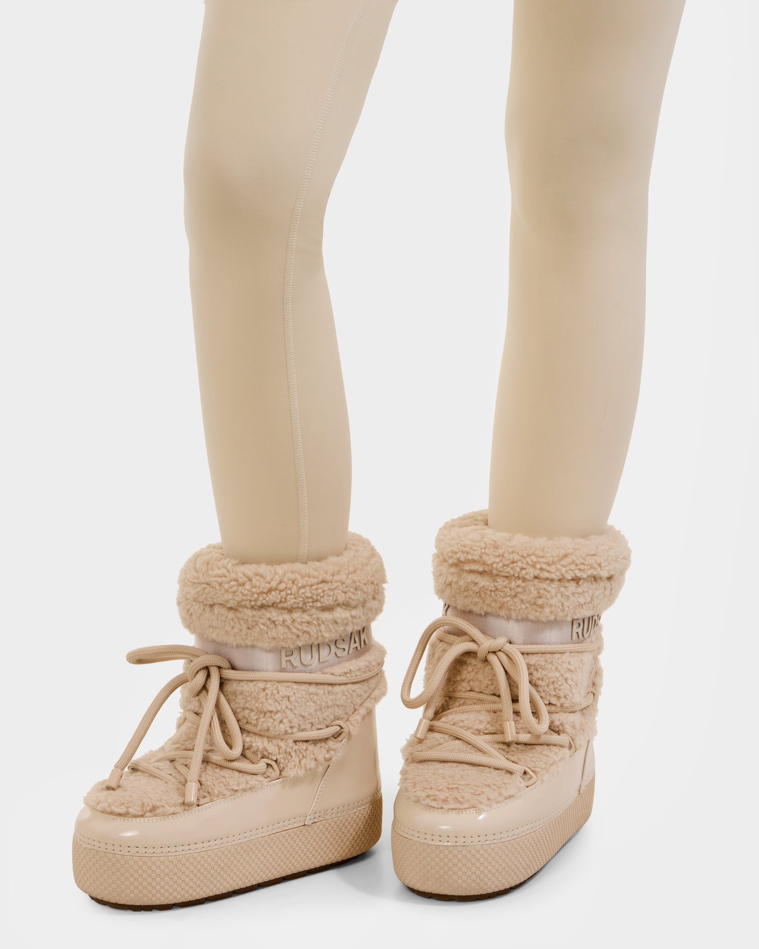 A person wearing cream-colored leggings and Rudsak KATHY - 8223513 Vanilla faux shearling moon boots with thick soles and laces, shown on a white background.