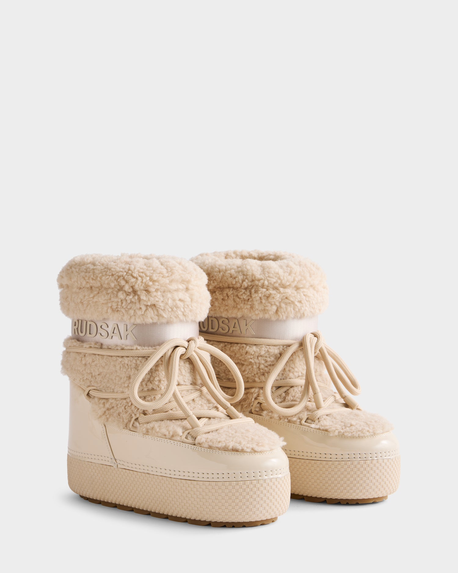 The KATHY - 8223513 Vanilla by Rudsak are beige women’s winter boots with a thick rubber sole, lace-up front, faux shearling trim, and water-repellent finish, featuring the Rudsak logo on the ankle band.