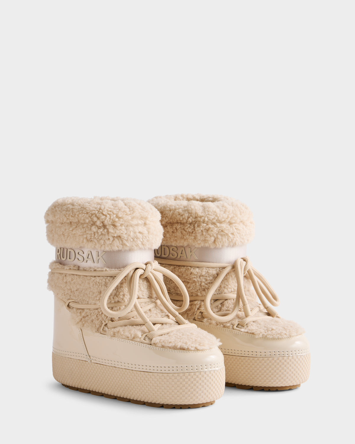The KATHY - 8223513 Vanilla by Rudsak are beige women’s winter boots with a thick rubber sole, lace-up front, faux shearling trim, and water-repellent finish, featuring the Rudsak logo on the ankle band.