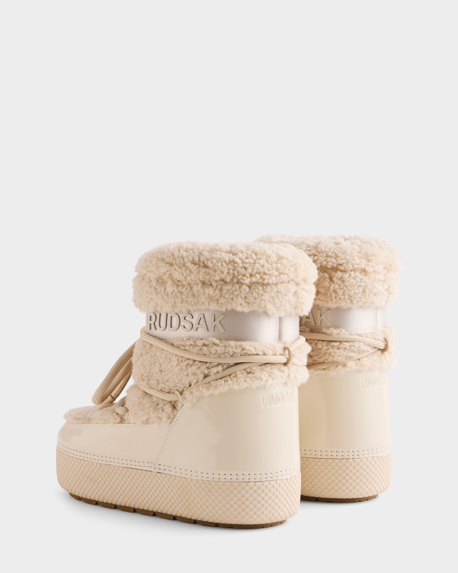 Two beige women’s KATHY - 8223513 Vanilla winter boots by Rudsak with fluffy sherpa lining, shiny textured soles, decorative laces, water-repellent finish, and RUDSAK branding on the back. Shown against a plain white background.