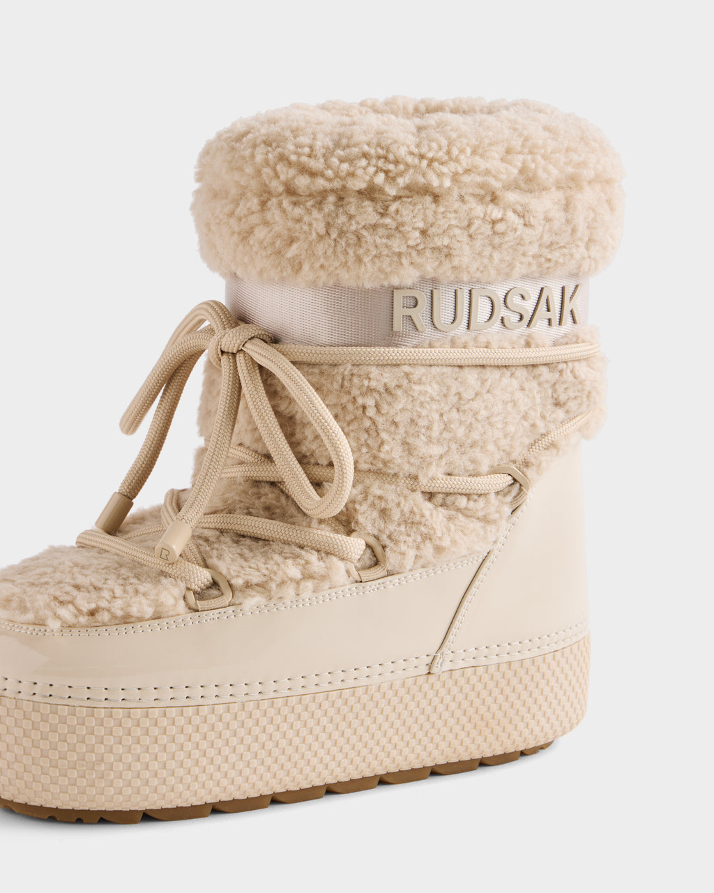 The KATHY - 8223513 Vanilla by Rudsak is a beige women’s winter boot with a thick faux shearling upper, lace-up front, ribbed sole, and Rudsak branding embossed on a band near the top.