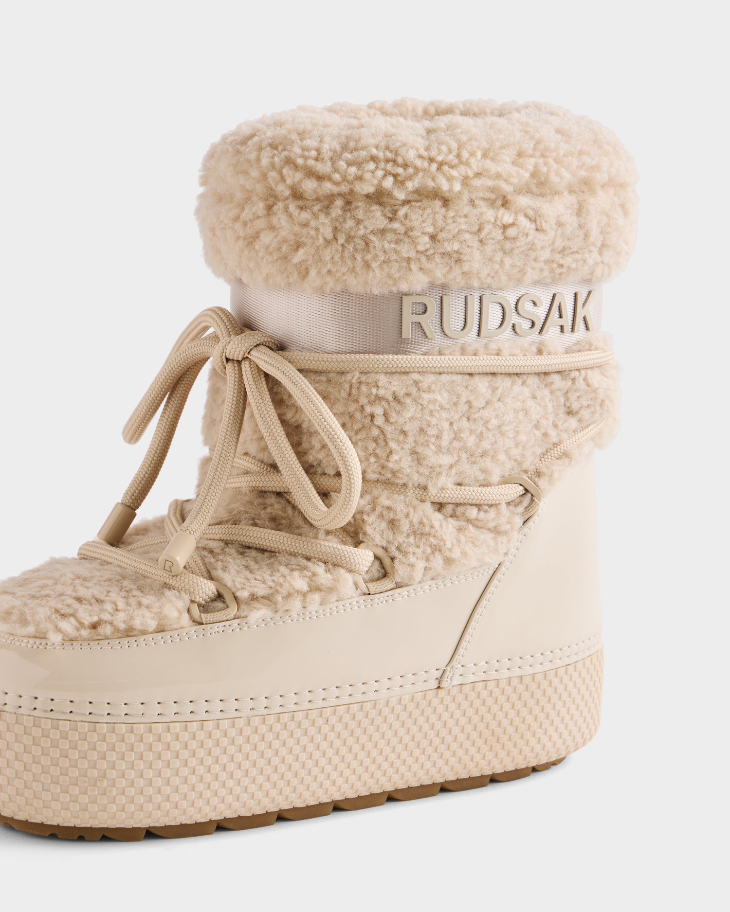 The KATHY - 8223513 Vanilla by Rudsak is a beige women’s winter boot with a thick faux shearling upper, lace-up front, ribbed sole, and Rudsak branding embossed on a band near the top.