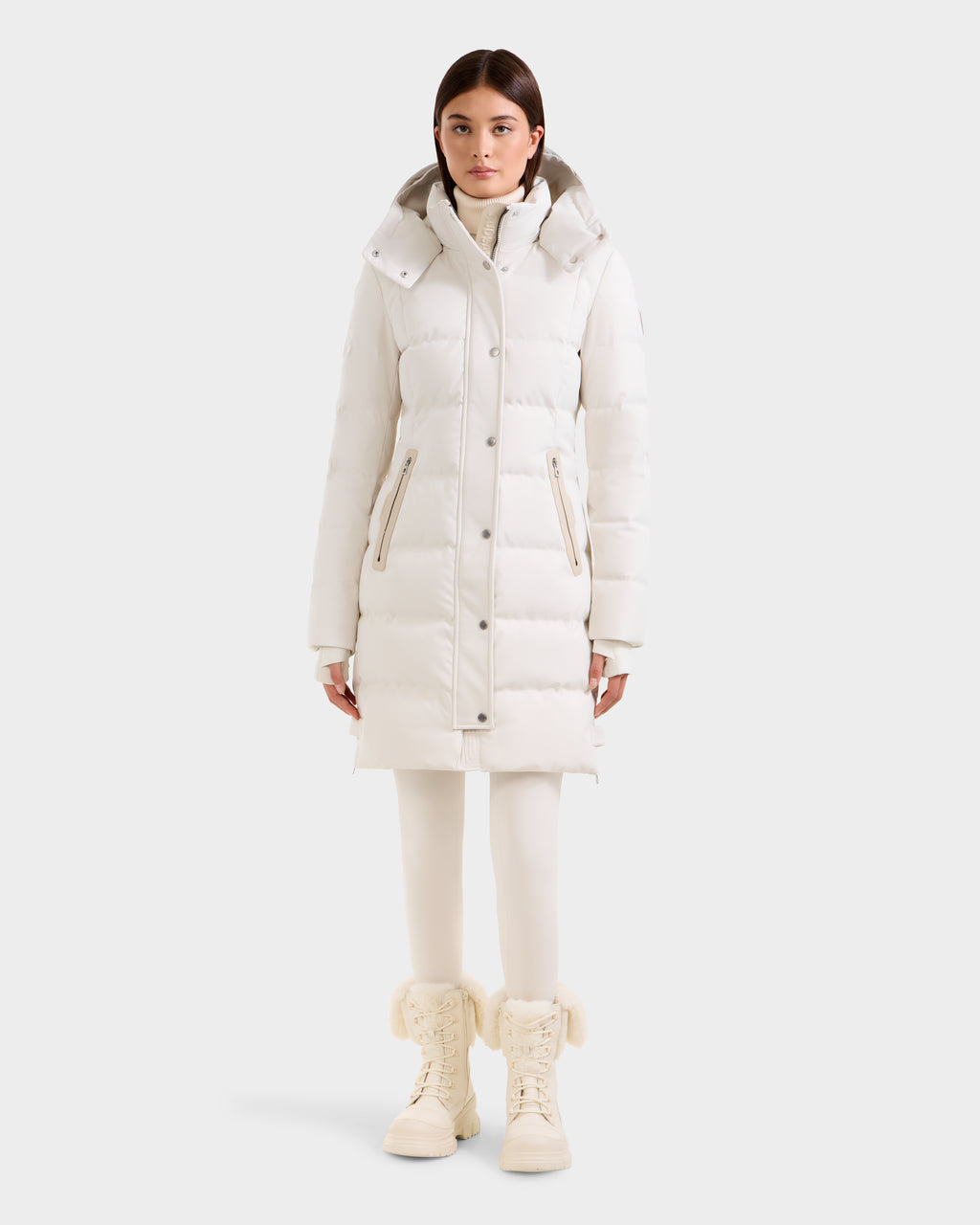 A woman stands facing forward in a long white Rudsak KEHLANI H - 8125643 Vanilla women’s down parka with RDS-certified down, white leggings, and cream fur-trimmed lace-up boots, against a plain light background.