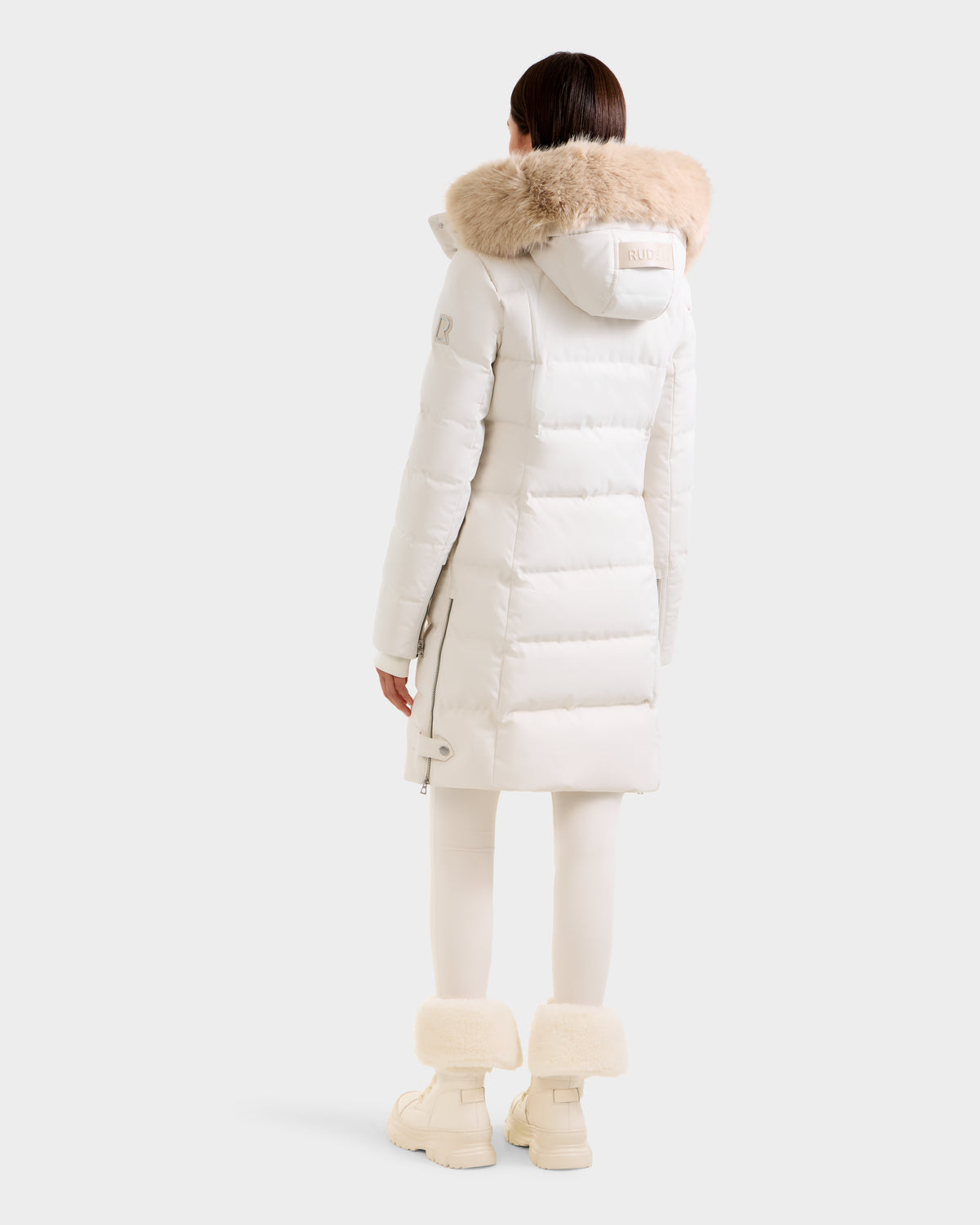 A person wearing the Rudsak KEHLANI H - 8125643 Vanilla women's down parka with fur-trimmed hood, matching leggings, and fur-cuffed boots stands facing away against a plain white background.