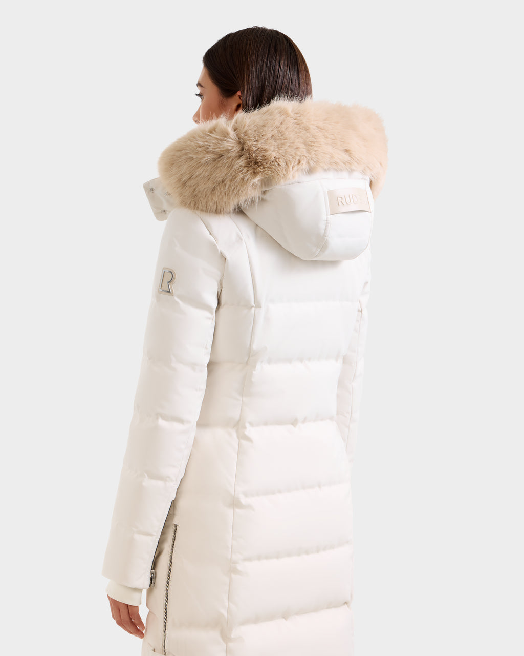 A woman is seen from behind in a Rudsak KEHLANI H - 8125643 Vanilla long white down parka with a large, fluffy light brown fur hood, set against a plain background.