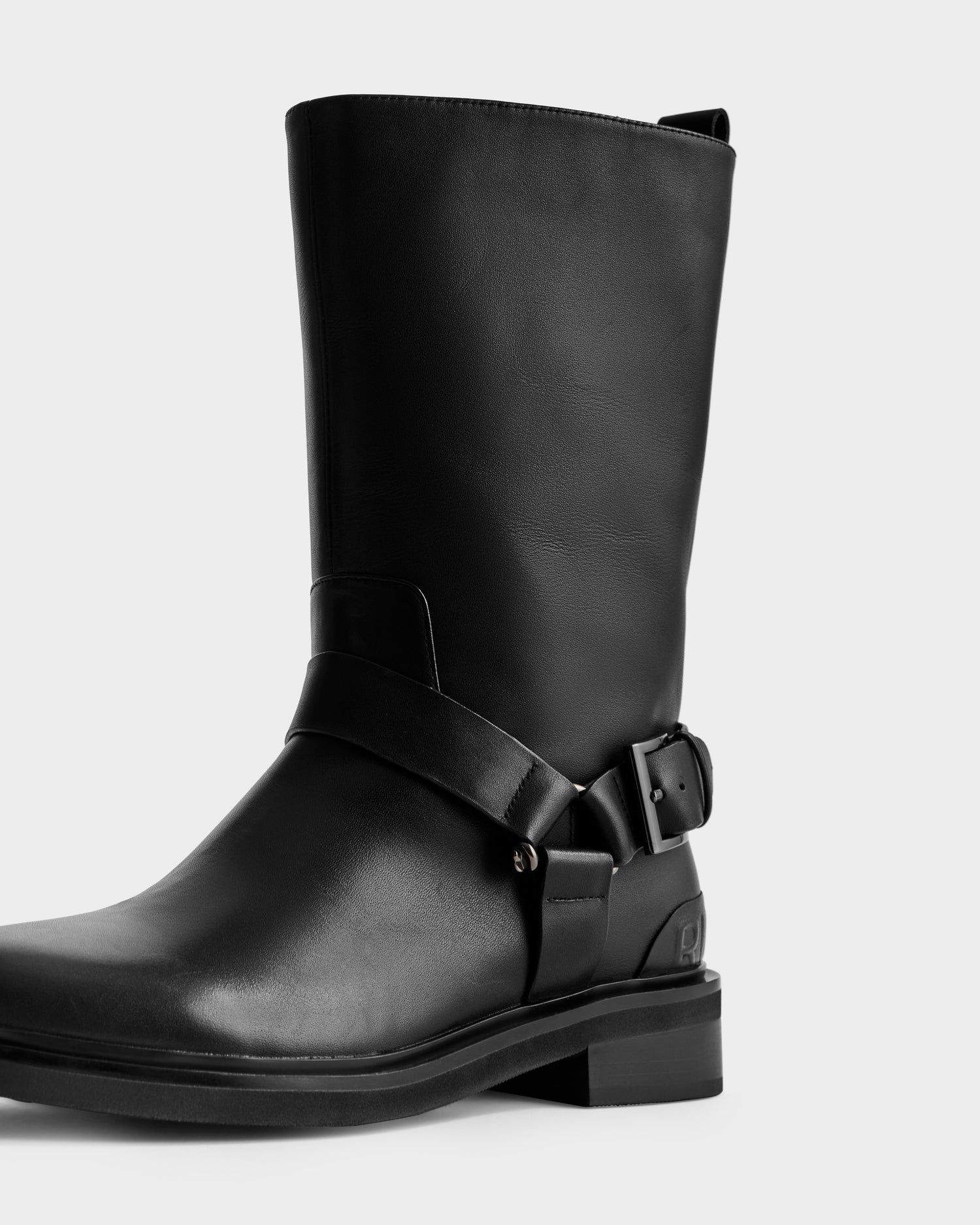 The KIRRA - 8225558 Black by Rudsak is a black leather mid-calf moto boot with a round toe, low stacked heel, and decorative side harness strap—an ideal addition to your women's fashion boots collection.