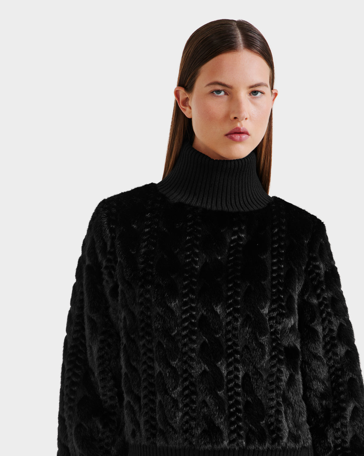 A woman with straight brown hair wears the Rudsak LAYLA F - 8525630 Black cable-knit-inspired turtleneck, looking forward with a neutral expression against a light backdrop, embodying modern après-ski style.