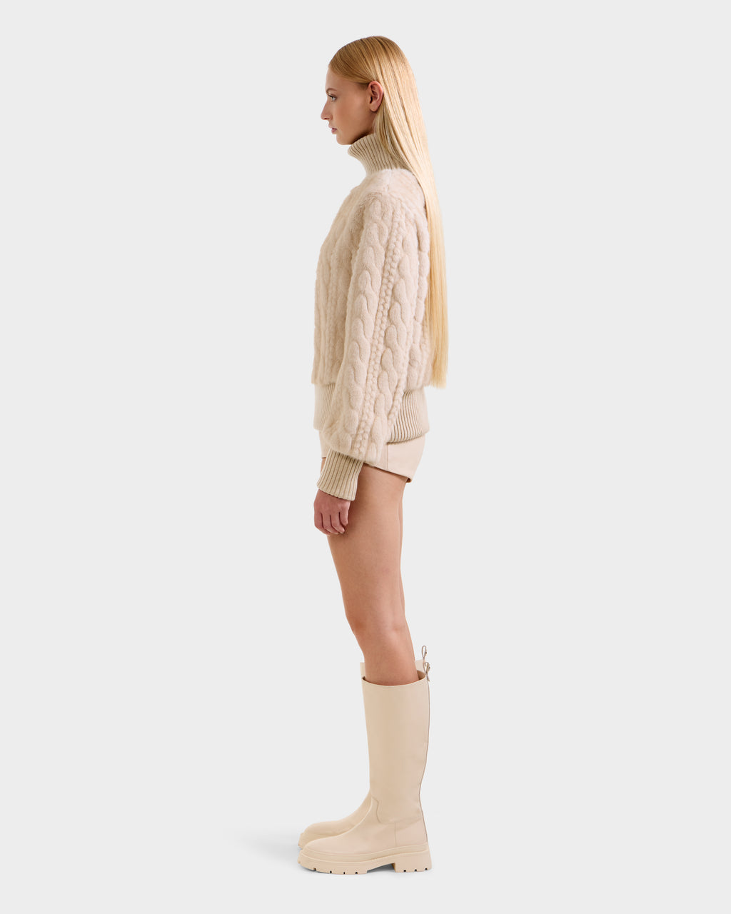 A woman in profile against a plain background wears the LAYLA F - 8525630 Vanilla sweater and matching shorts by Rudsak, styled with knee-high cream boots. She has long, straight blonde hair and a neutral expression.