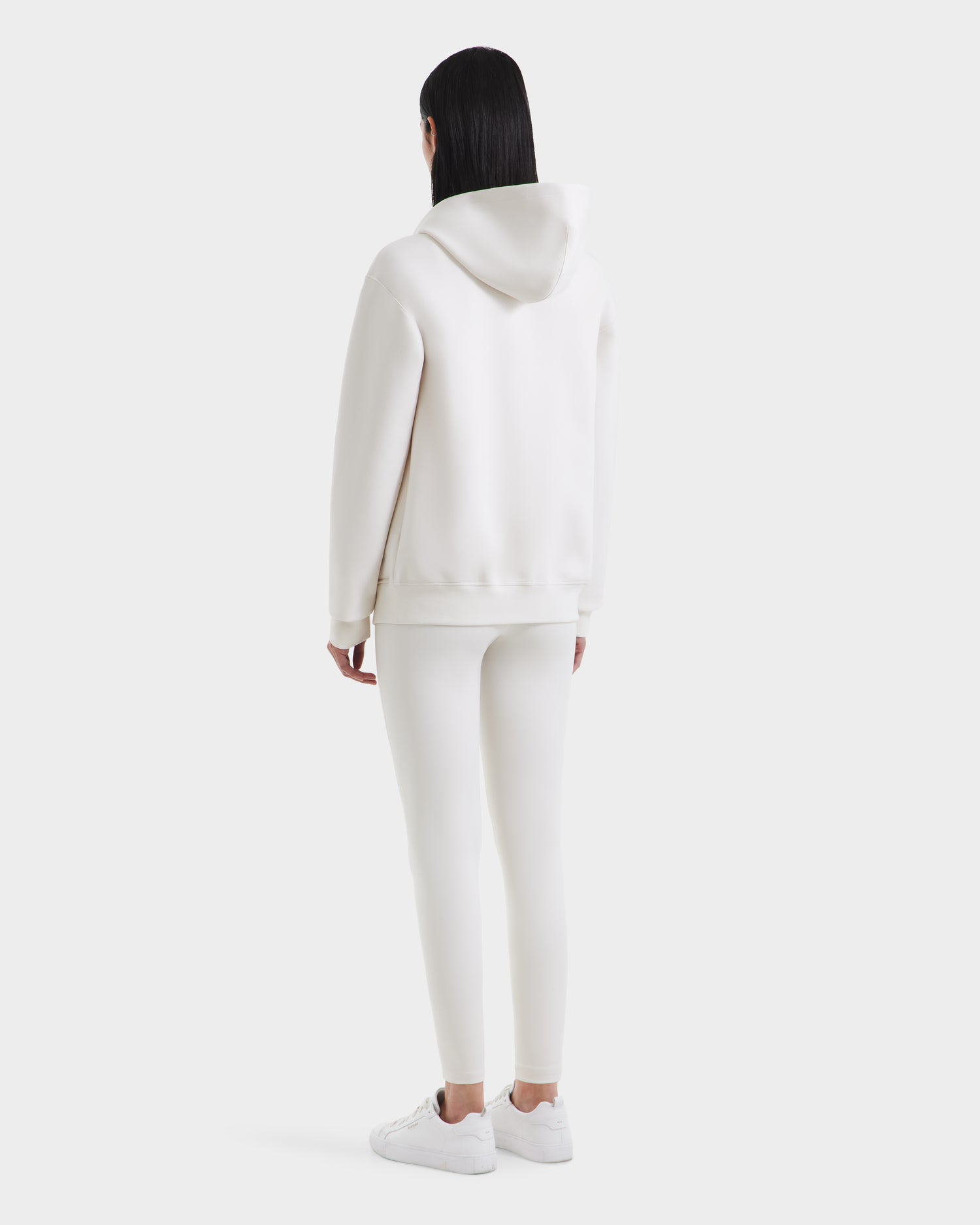 A person with straight dark hair, seen from behind, is wearing the Rudsak LEVI - 9525552 Vanilla W hoodie, fitted pants, and white sneakers against a plain light background.
