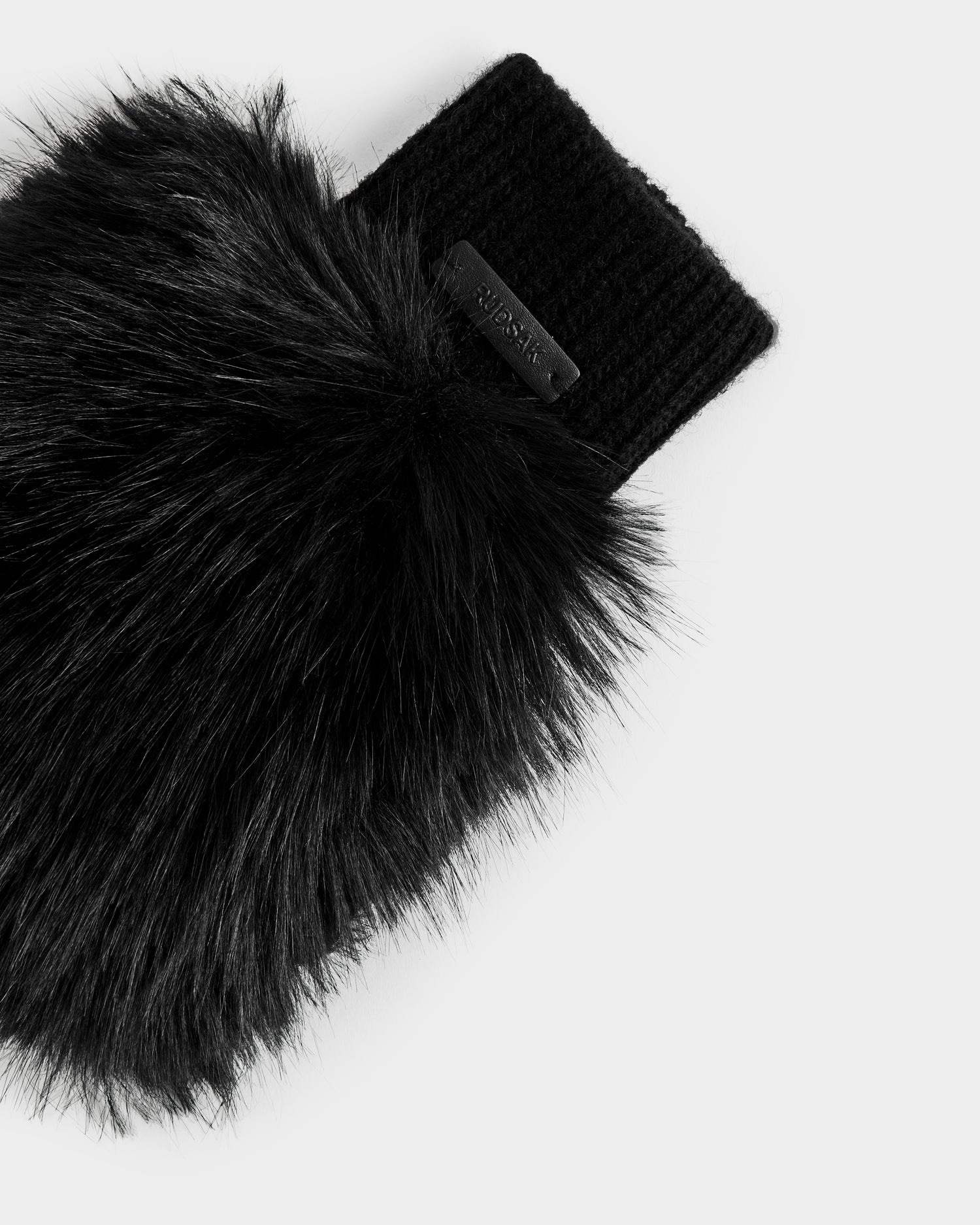 A close-up of the Rudsak LIA - 8425007 Black women’s fingerless mitten showcases black faux fur and a ribbed wool-blend knit cuff with a small black label, set against a plain light gray background.