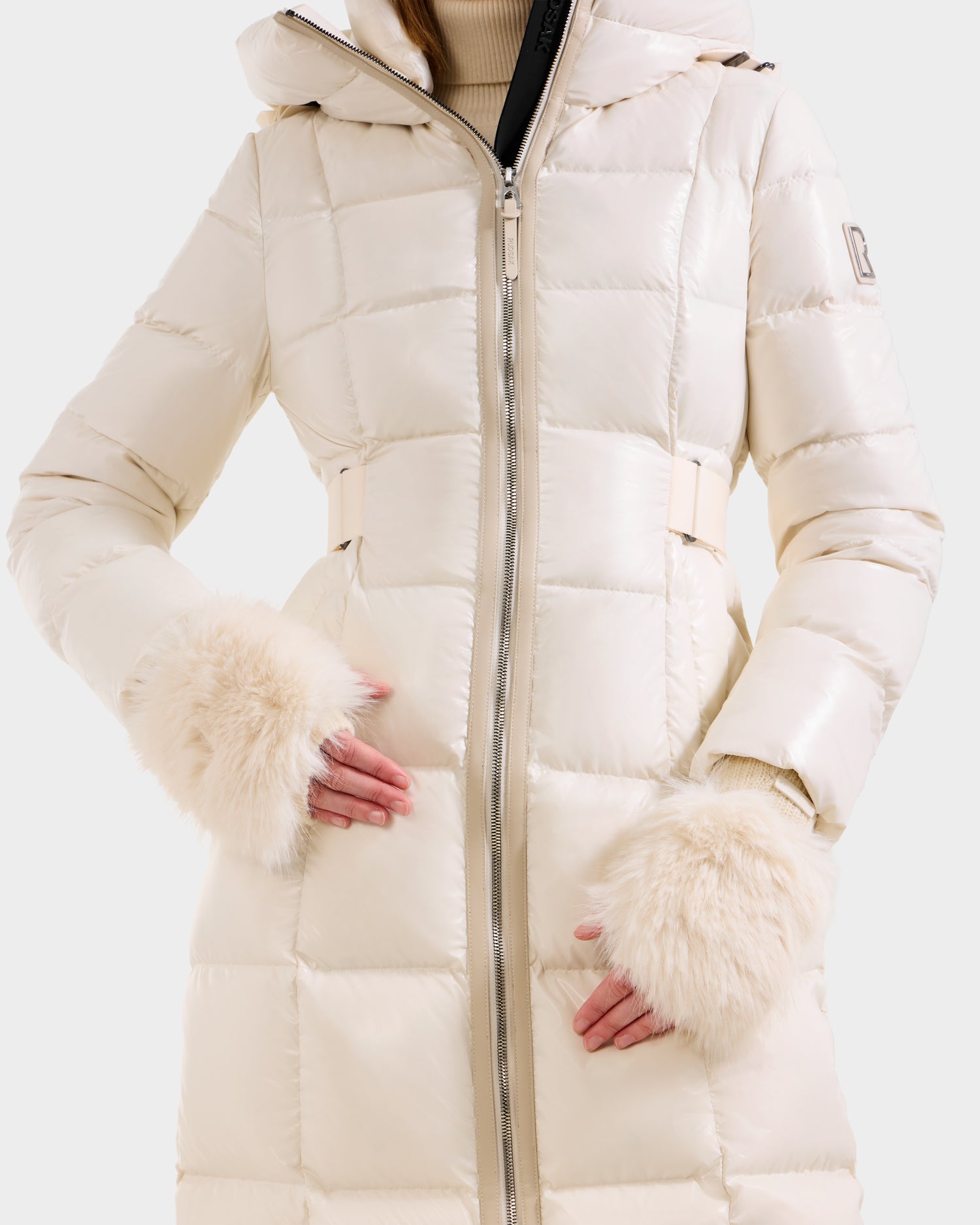 A person wears the Rudsak LIA - 8425007 Vanilla puffer coat with front zipper and faux fur cuffs, layered over a beige turtleneck sweater for a cozy, stylish look.