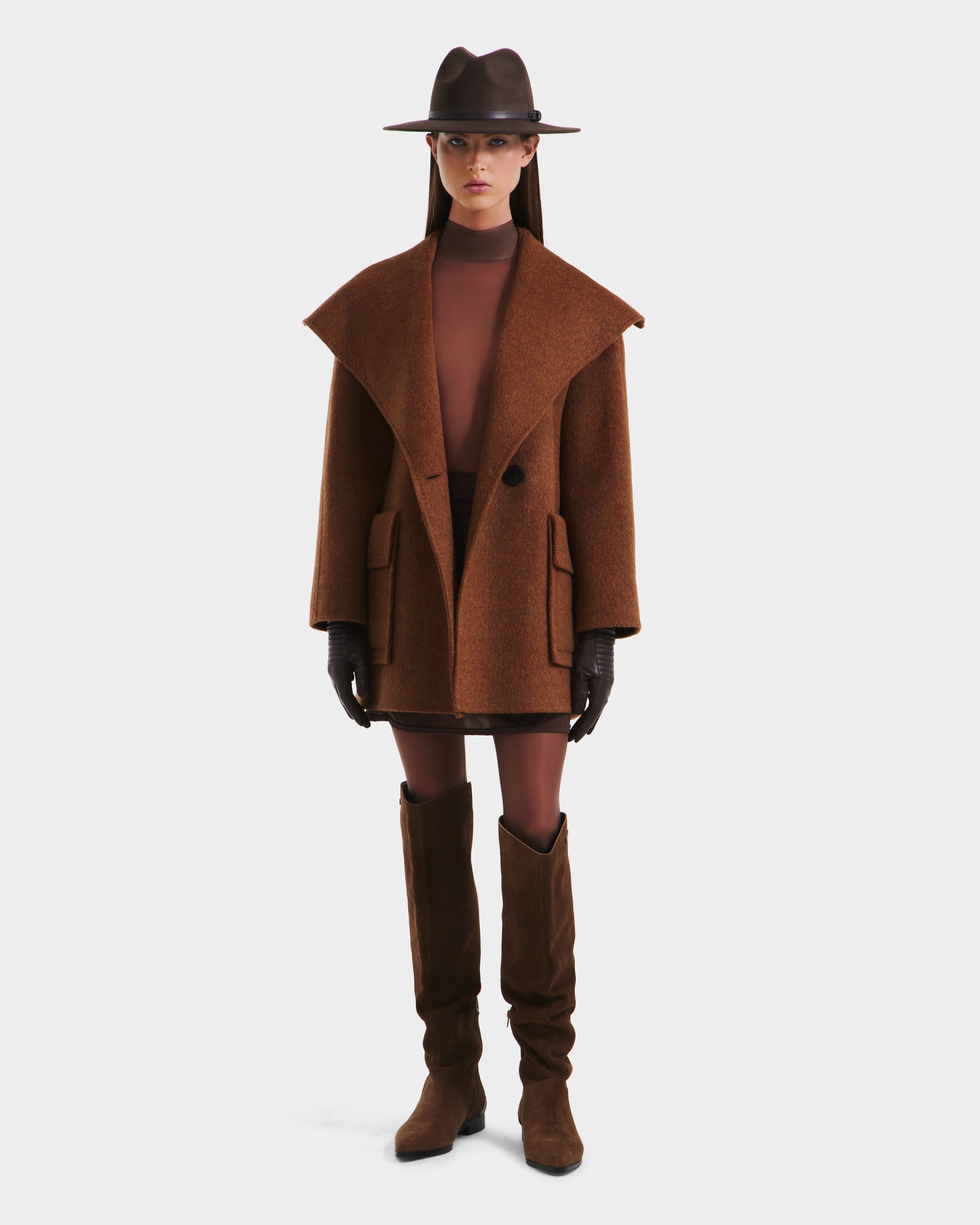 A woman in a Rudsak LUCIA - 8125633 Camel wool jacket and wide-brimmed brown hat faces forward against a plain white background, styled with brown gloves, vegan leather belt, mini skirt, tights, and knee-high boots.