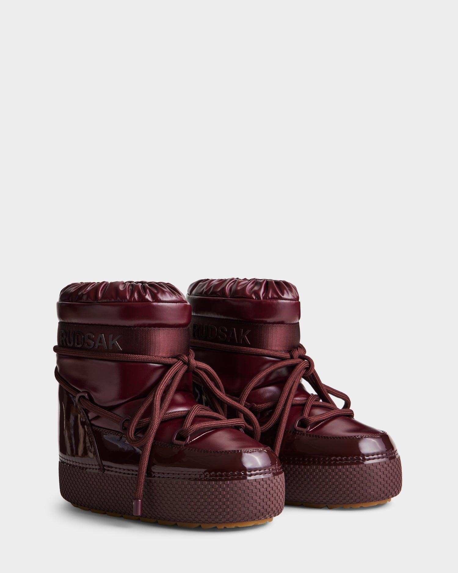 MACE - 8223500 Bordeaux by Rudsak: women’s shiny burgundy short moon boots with thick soles, rounded toes, lace-up fronts, puffy insulated design, faux fur lining, and Rudsak branding on the upper cuff.