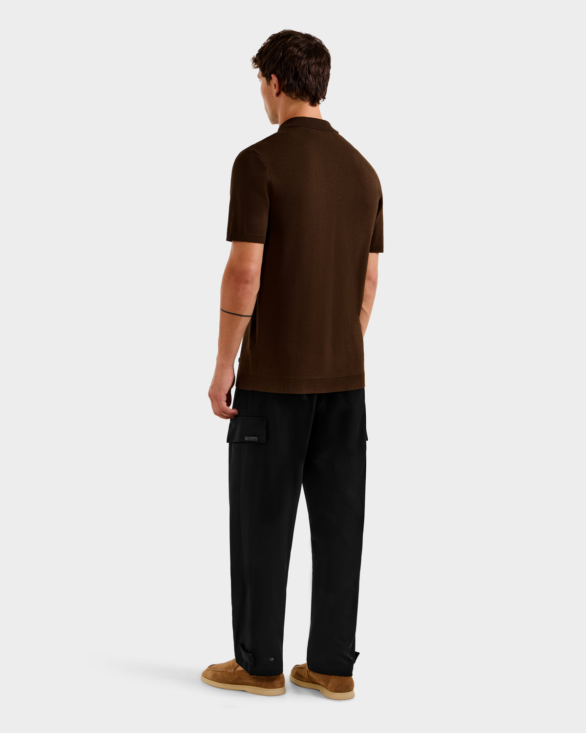 A person stands facing away, showcasing the Rudsak MAISEN - 6524518 Mocha men's knit polo with black cargo pants and brown shoes against a plain light gray background—an effortless choice for the modern wardrobe.