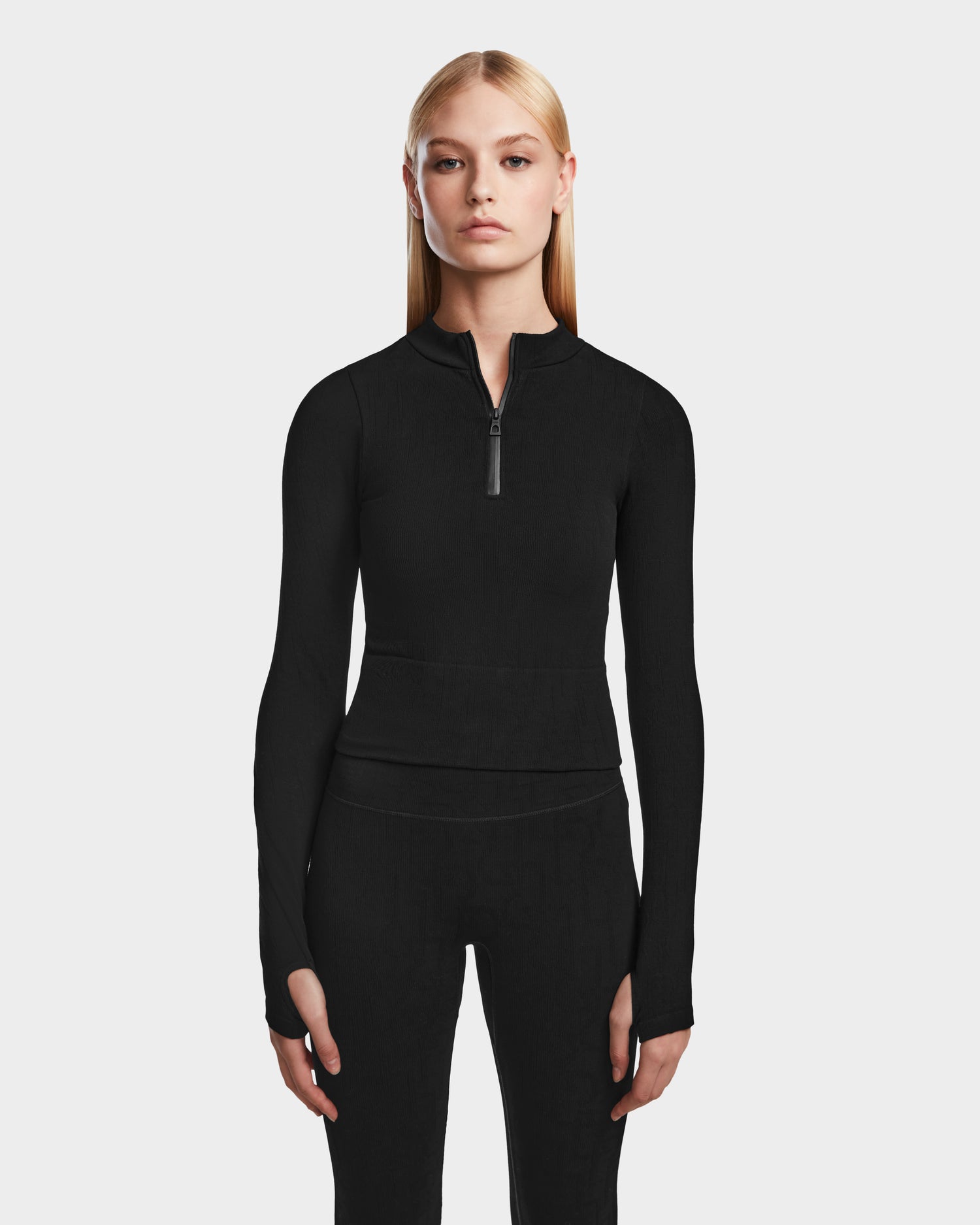 A woman with long blonde hair wears the Rudsak MARIAN - 8524513 Monogram Print Black top and matching black pants, standing against a light gray background—a sleek choice for any winter wardrobe.