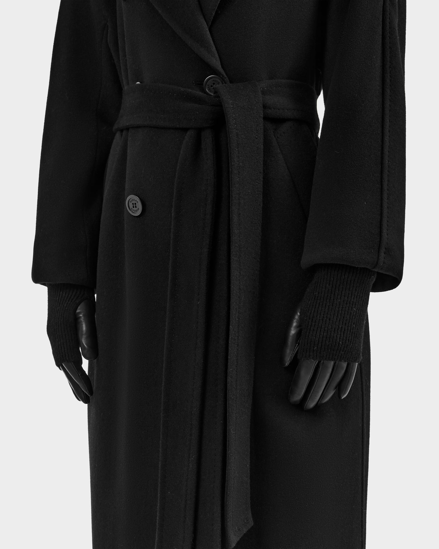 Model wears the Rudsak MARINE - 8424516 Black long belted coat with black knit wool gloves, styled for fall. Shown from neck to knees against a plain light background.