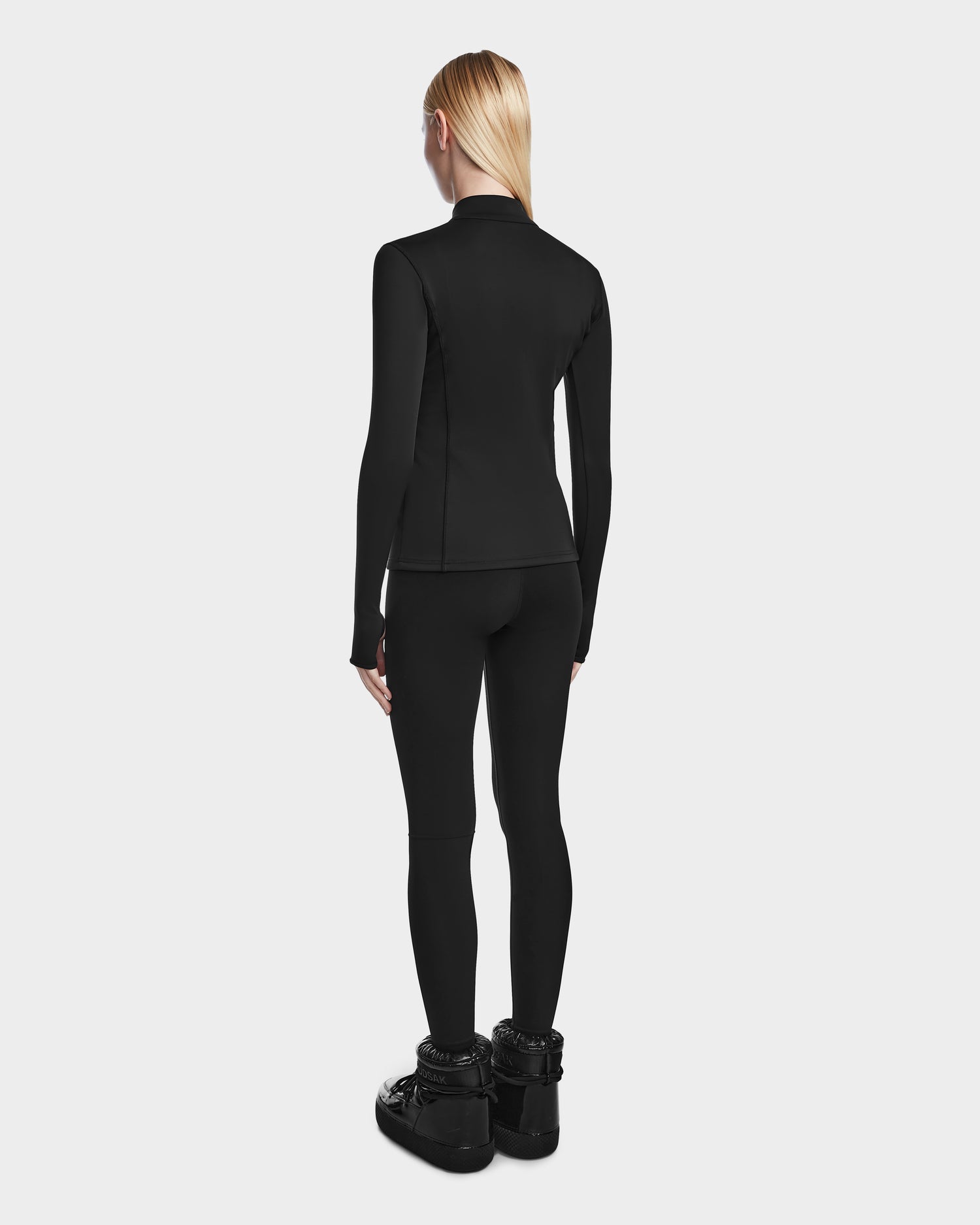 Wearing Rudsaks MARIS - 8524603 Black winter boots, a person with long blonde hair stands facing away against a light gray background—perfect for ski layering or winter sports.