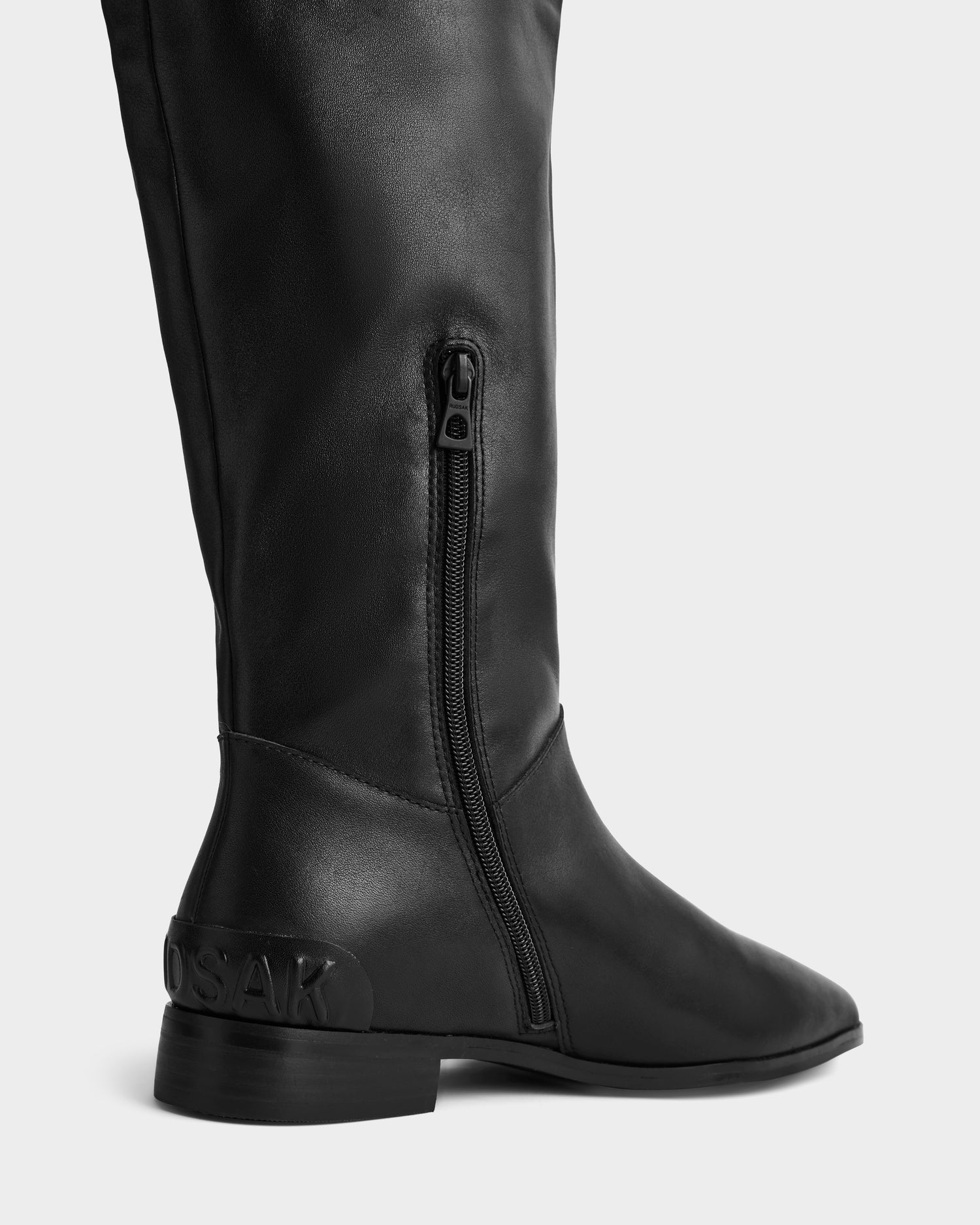 Close-up side view of the Rudsak MARSALLA - 8225033 Black women’s leather high-shaft boot with a low heel, side zipper, and "OSAK" embossed on the back near the heel, shown against a plain light background.