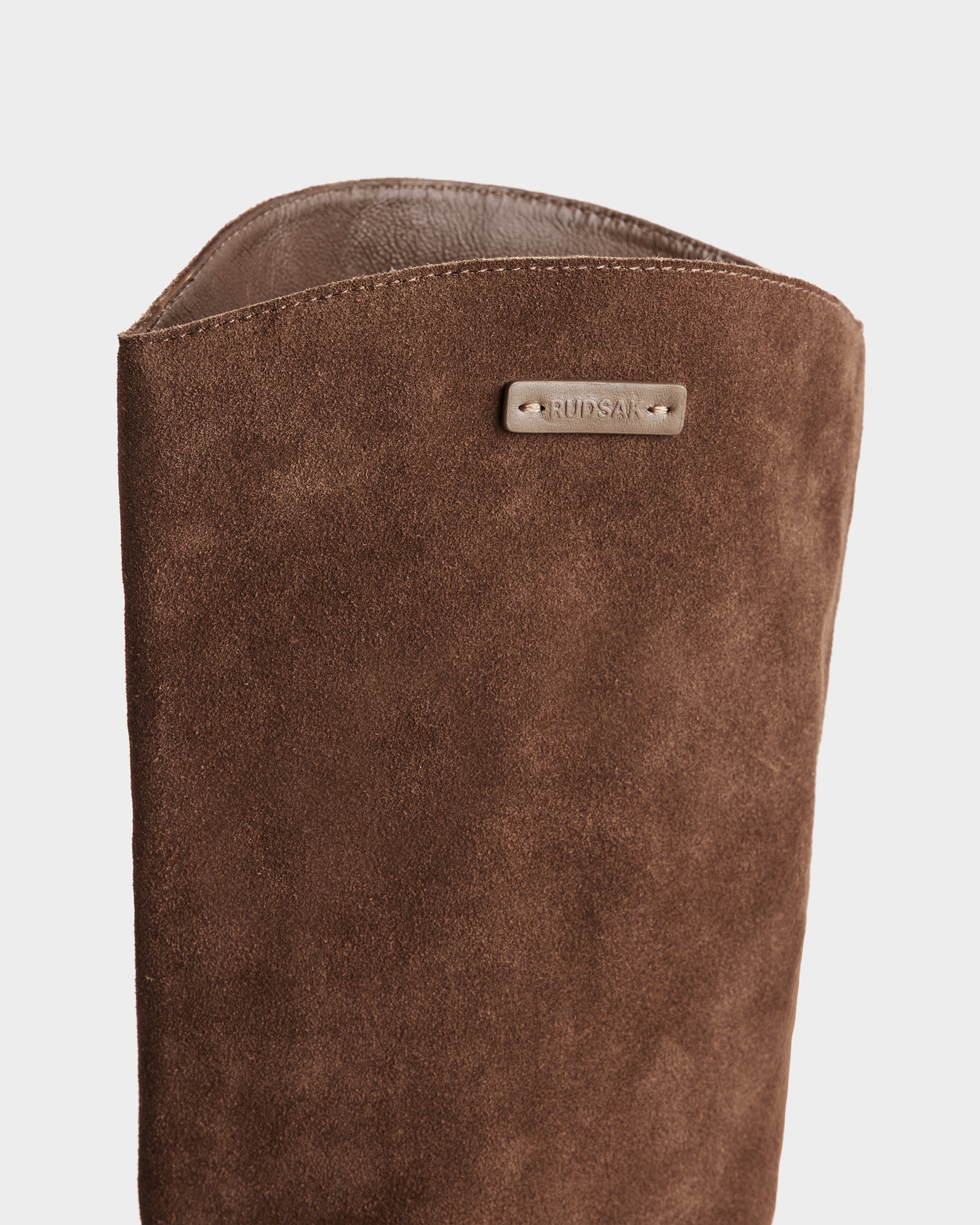 Close-up of the upper part of the MARSALLA - 8225033 Mocha women’s suede riding boot by Rudsak, featuring a high-shaft design and a small metallic RUDSAK tag, set against a plain white background.