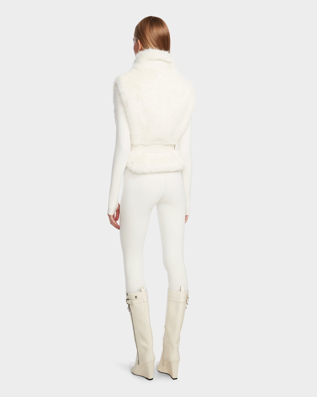 A person with straight, reddish-brown hair is seen from behind, wearing Rudsak’s MAULIN - 8524611 Iceland: a faux fur vest over a fitted long-sleeve top, slim pants, and knee-high wedge-heeled vegan leather boots with buckles.