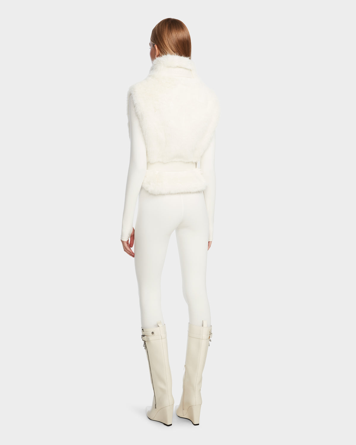 A person with straight, reddish-brown hair is seen from behind, wearing Rudsak’s MAULIN - 8524611 Iceland: a faux fur vest over a fitted long-sleeve top, slim pants, and knee-high wedge-heeled vegan leather boots with buckles.