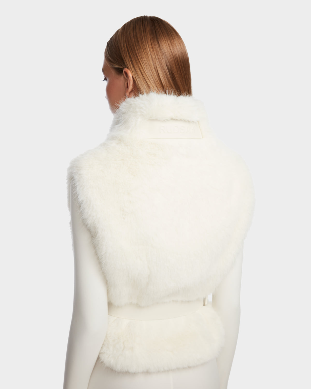 A person with straight, light brown hair models the Rudsak MAULIN - 8524611 Iceland faux fur vest over a white long-sleeve top, shown from the back against a plain light background.