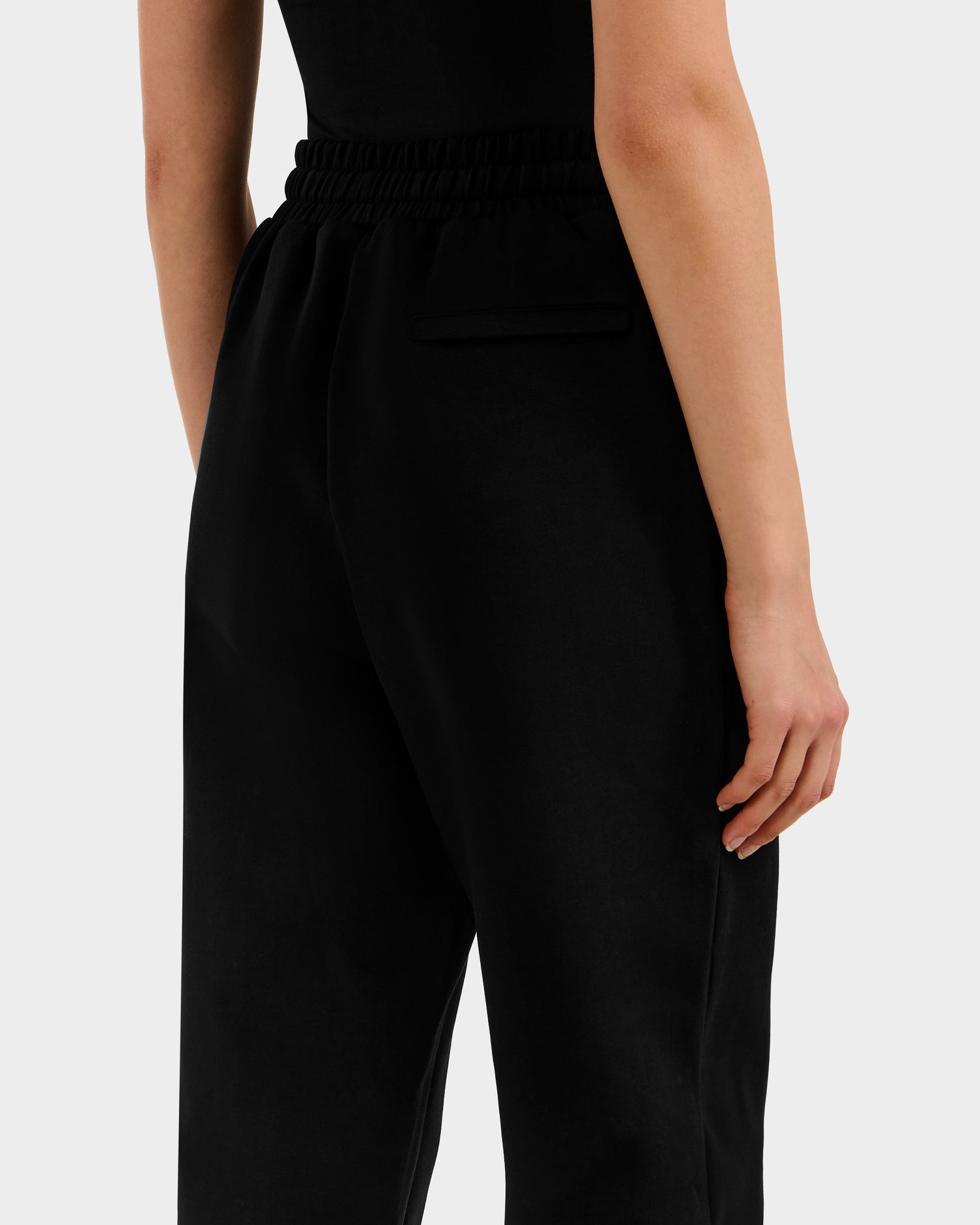 A person wears Rudsak's MAXTON - U525007 Black W unisex cotton-blend jogger pants with an elastic waistband and back pocket, shown from the waist down—one hand by their side, the other partially in a pocket.