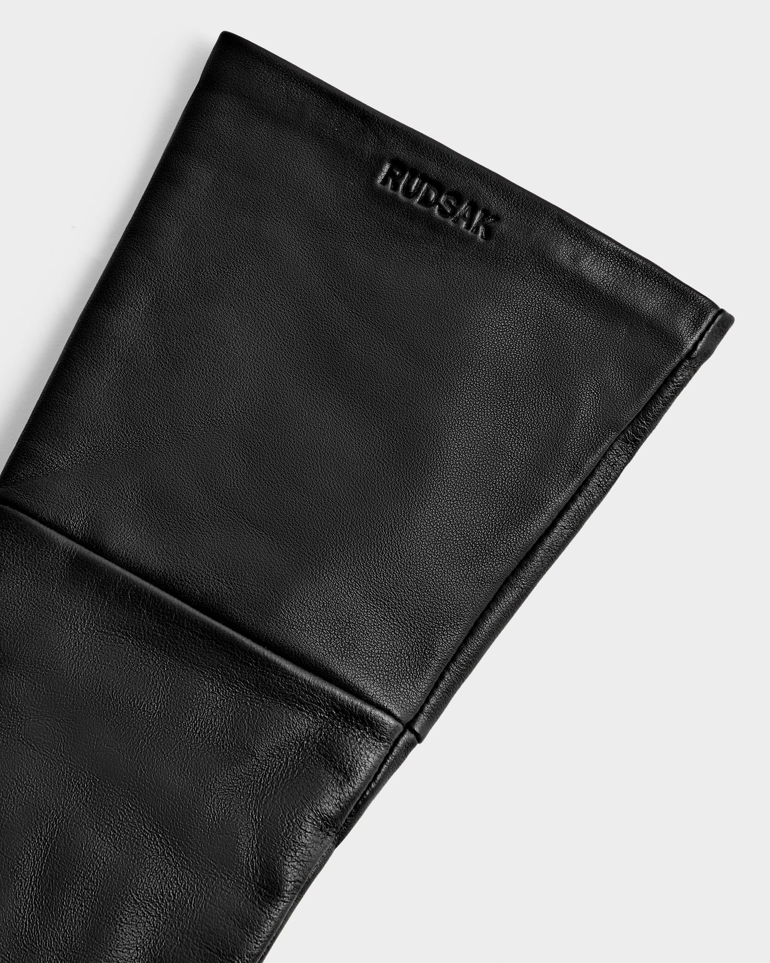 Close-up of the black MEGAN - 8425541 glove by Rudsak with visible stitching and an embossed logo on the top cuff, set against a white background—a sleek women's accessory that's also touchscreen-compatible.