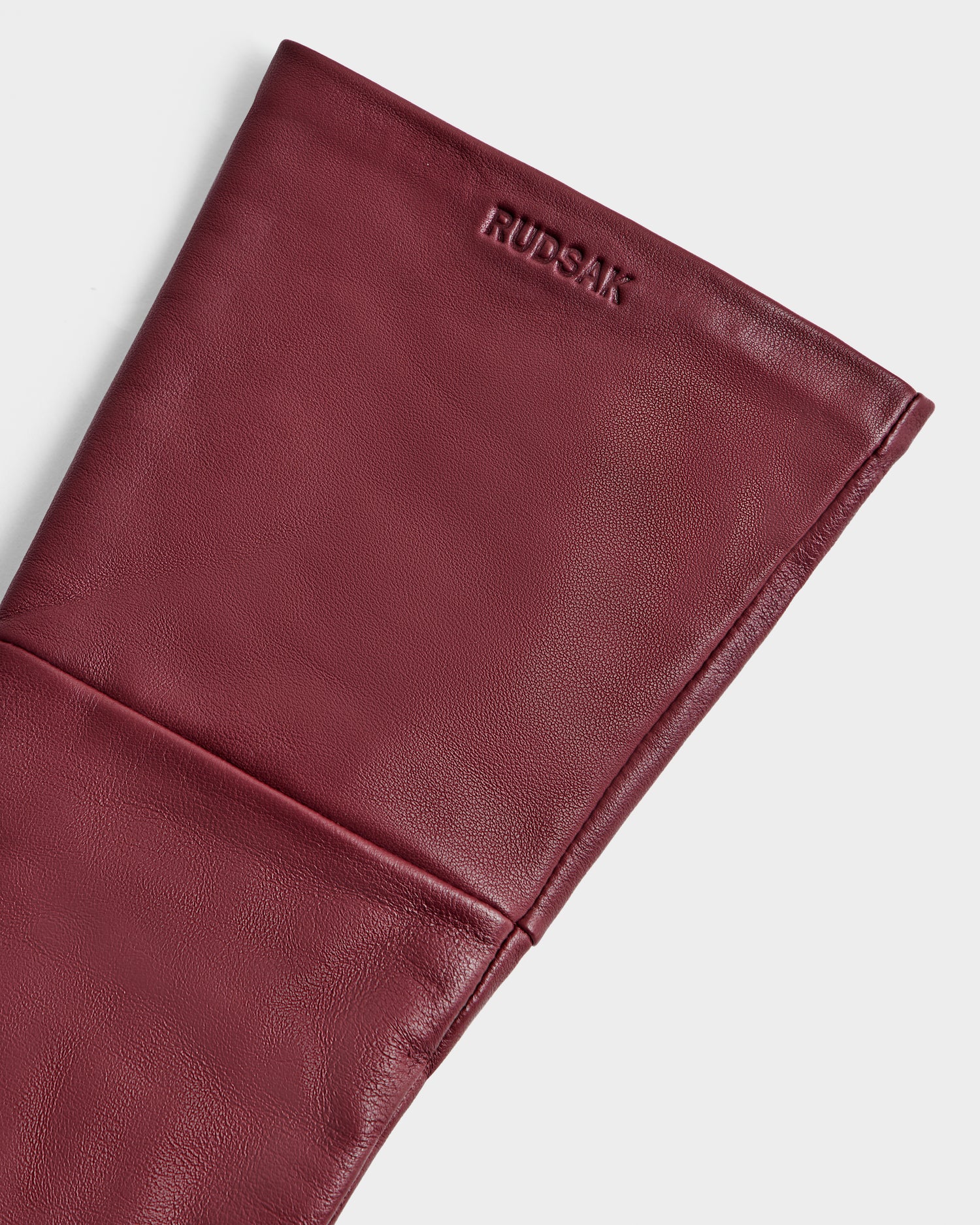 Close-up of the Rudsak MEGAN - 8425541 Bordeaux, a burgundy leather women’s accessory with the brand name embossed near the top. Smooth leather texture and visible stitching enhance its elegant look.