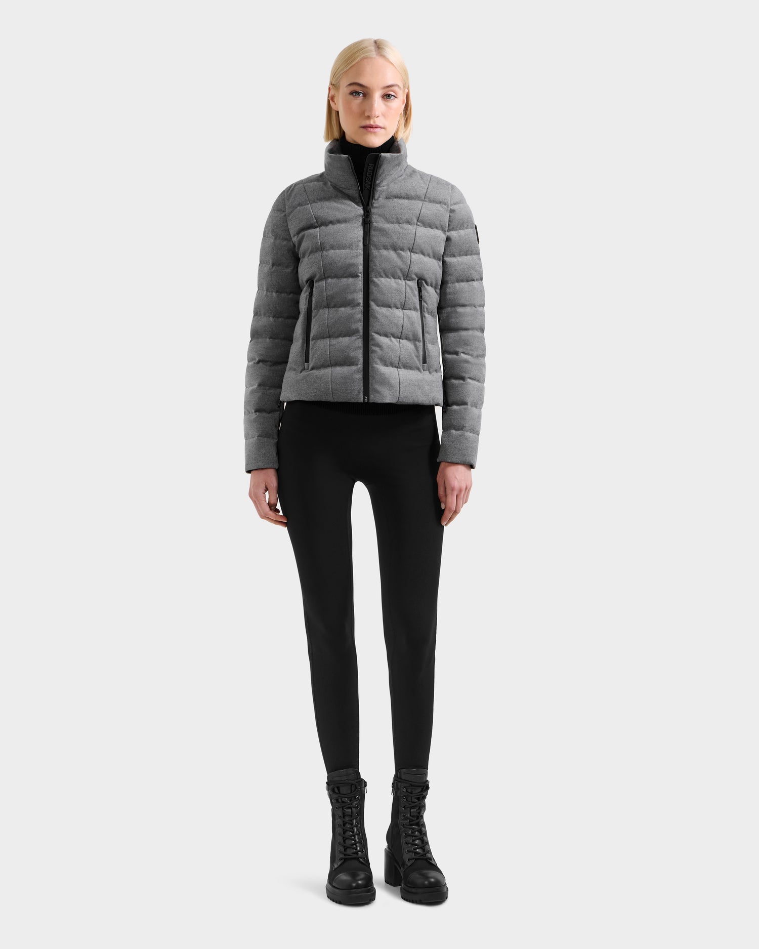 A woman faces forward wearing the Rudsak MELISSA W - 8125564 Heather Charcoal lightweight down jacket with a wool-blend shell, paired with black leggings and lace-up boots, set against a plain light gray background.