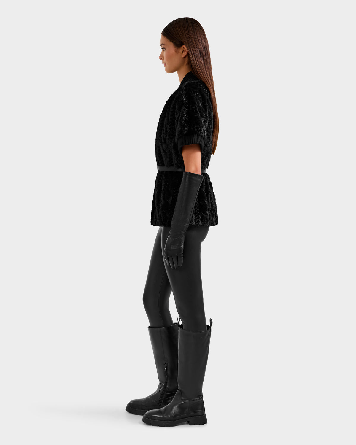A woman stands in profile wearing the Rudsak MENDOTA F - 8525561 Black top, long black gloves, black leggings, and knee-high boots against a plain light gray background.