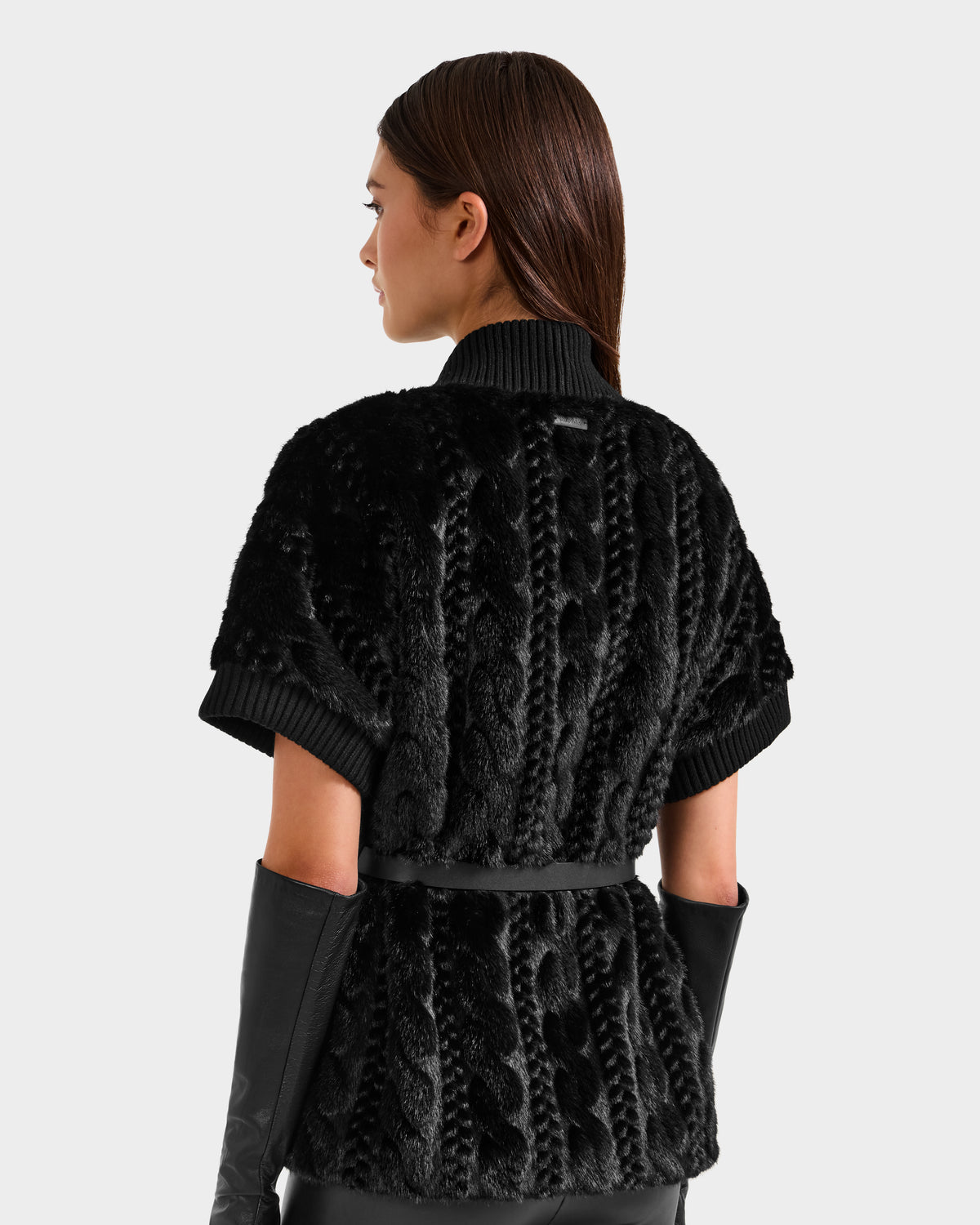 A woman with straight brown hair is seen from the back in a Rudsak MENDOTA F - 8525561 black textured short-sleeve sweater with a ribbed collar and belt, paired with long black gloves against a plain light background.