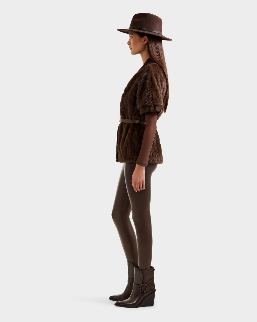 A woman in profile wears the RUDSAK MENDOTA F - 8525561 Mocha short brown textured jacket with a belt, paired with a wide-brimmed brown hat, brown leggings, and ankle-high brown heeled boots against a plain white background.