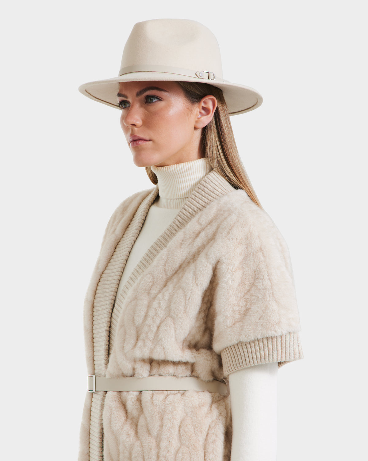 A woman models the Rudsak MENDOTA F - 8525561 Vanilla textured short-sleeved coat with vegan leather belt, paired with a beige hat and cream turtleneck, against a white background.