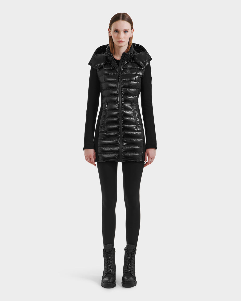 A woman faces forward against a plain white background, wearing the Rudsak MERINA C - 8125648 Black quilted down jacket over black leggings and lace-up boots.