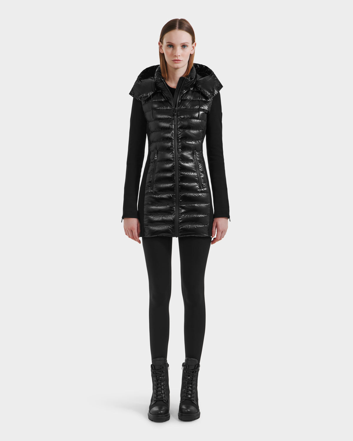 A woman faces forward against a plain white background, wearing the Rudsak MERINA C - 8125648 Black quilted down jacket over black leggings and lace-up boots.