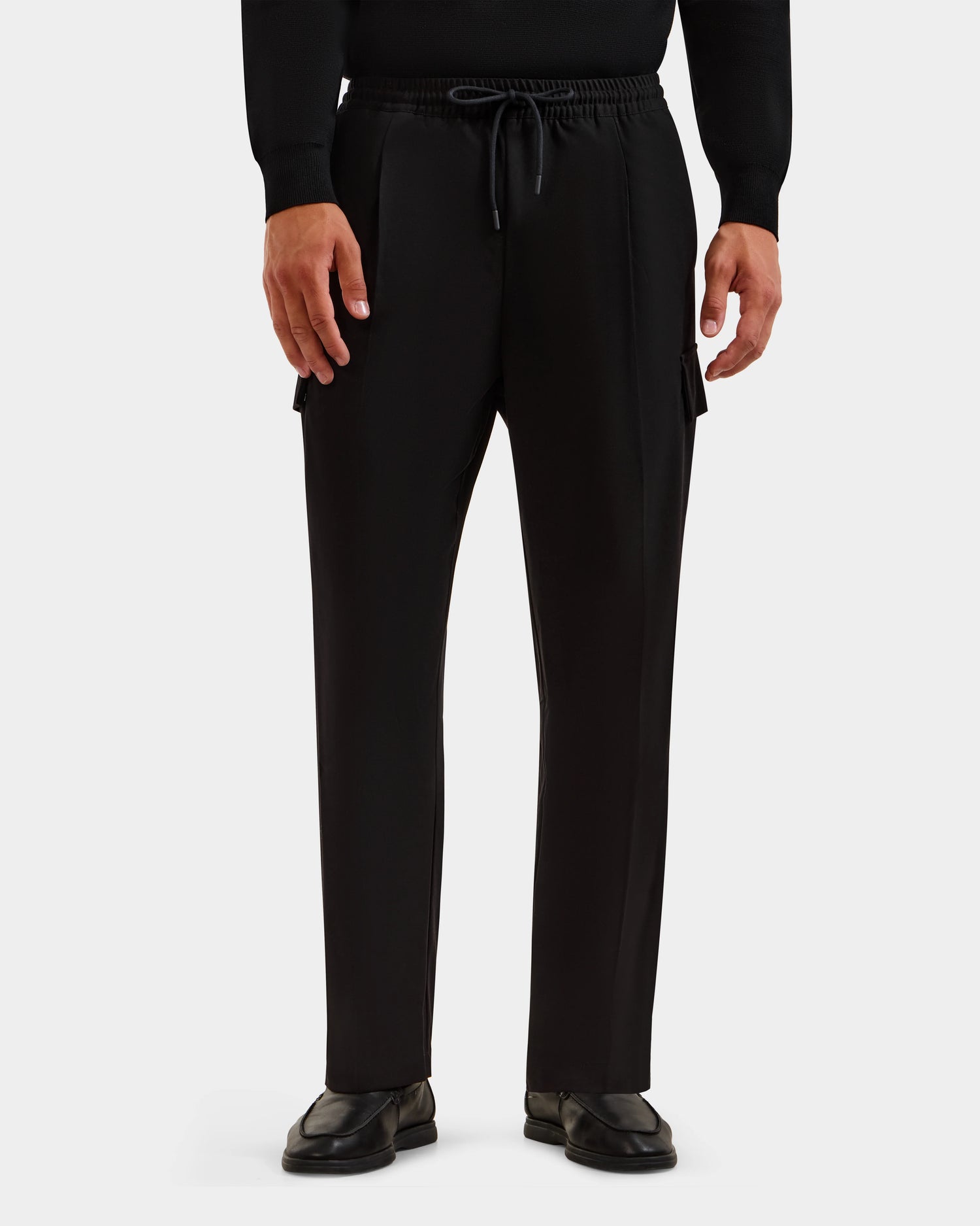 A person wears Rudsak’s MIKEY - 6525597 Black men’s trousers with a relaxed fit and side pockets, styled with a black long-sleeve shirt and shoes, standing against a plain white background.