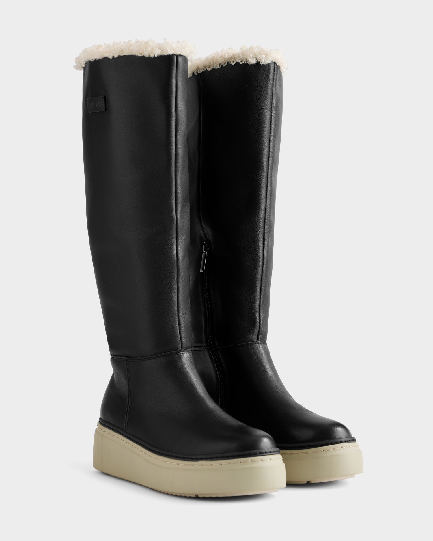 The Rudsak MIKIE L - 8225580 Black women’s leather boots feature cream platform soles and visible white shearling lining at the top, styled as chic foldover boots against a light background.