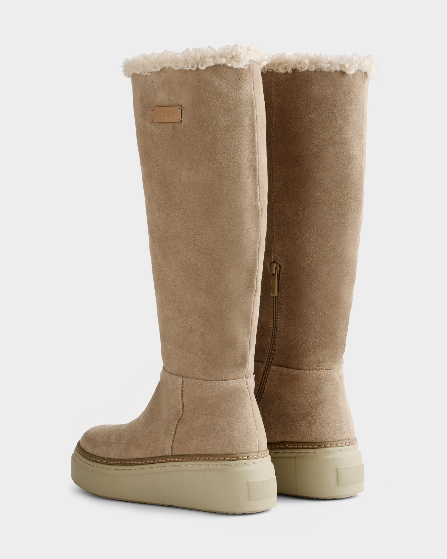 The MIKIE - 8225579 Almond boots by Rudsak are tall, tan suede with cream shearling trim and chunky light beige rubber soles, pictured from the rear and side.