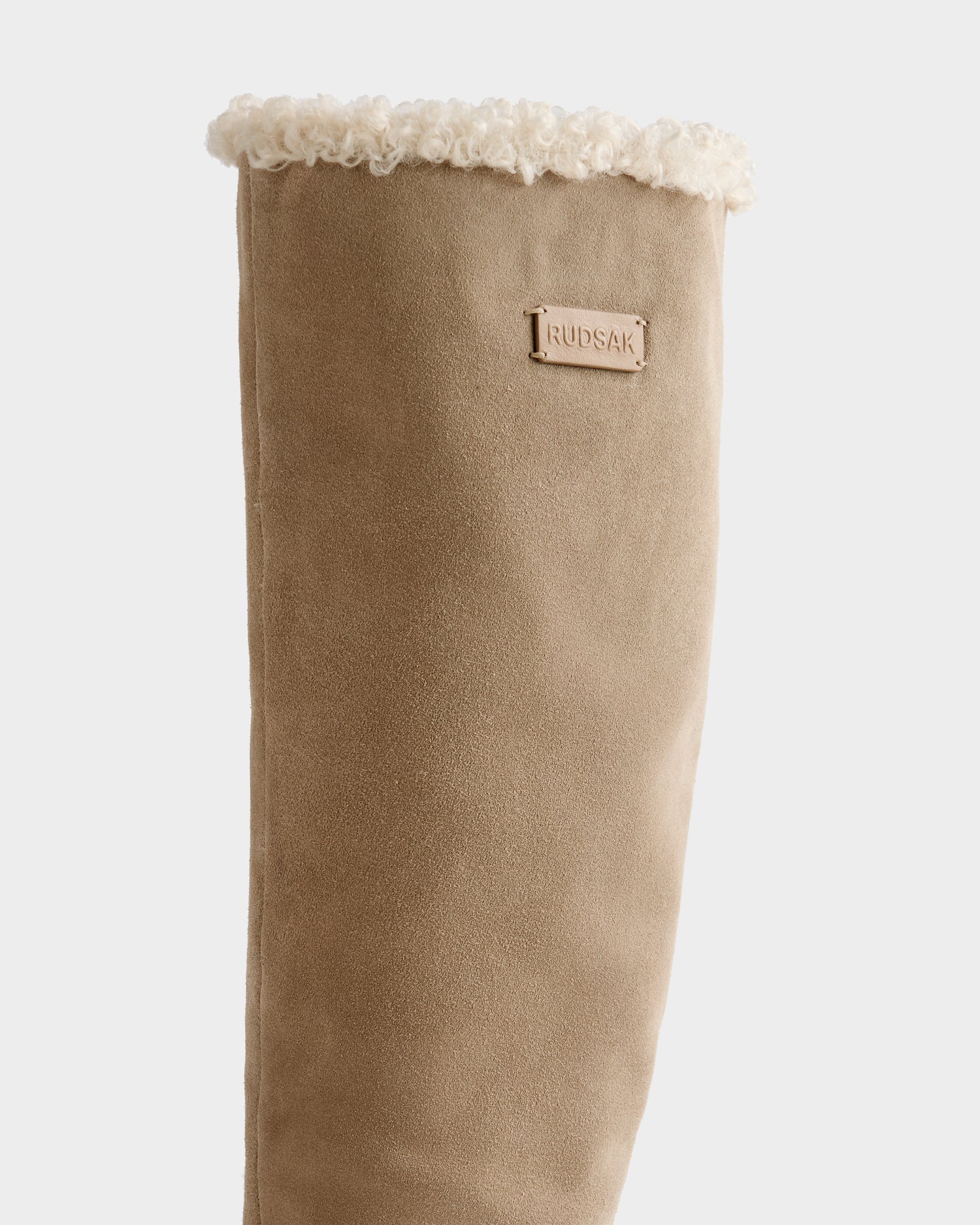 A close-up of the Rudsak MIKIE - 8225579 Almond boot in tan suede, featuring a soft white shearling lining at the top and a small Rudsak tag on the side.