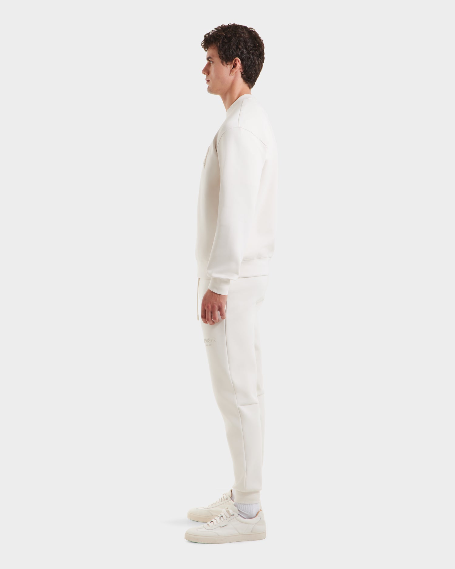 A man stands in profile against a white background, wearing the Rudsak MILOS - 6525646 Vanilla men’s crewneck sweatshirt made from a premium cotton blend. He faces right with arms relaxed at his sides.