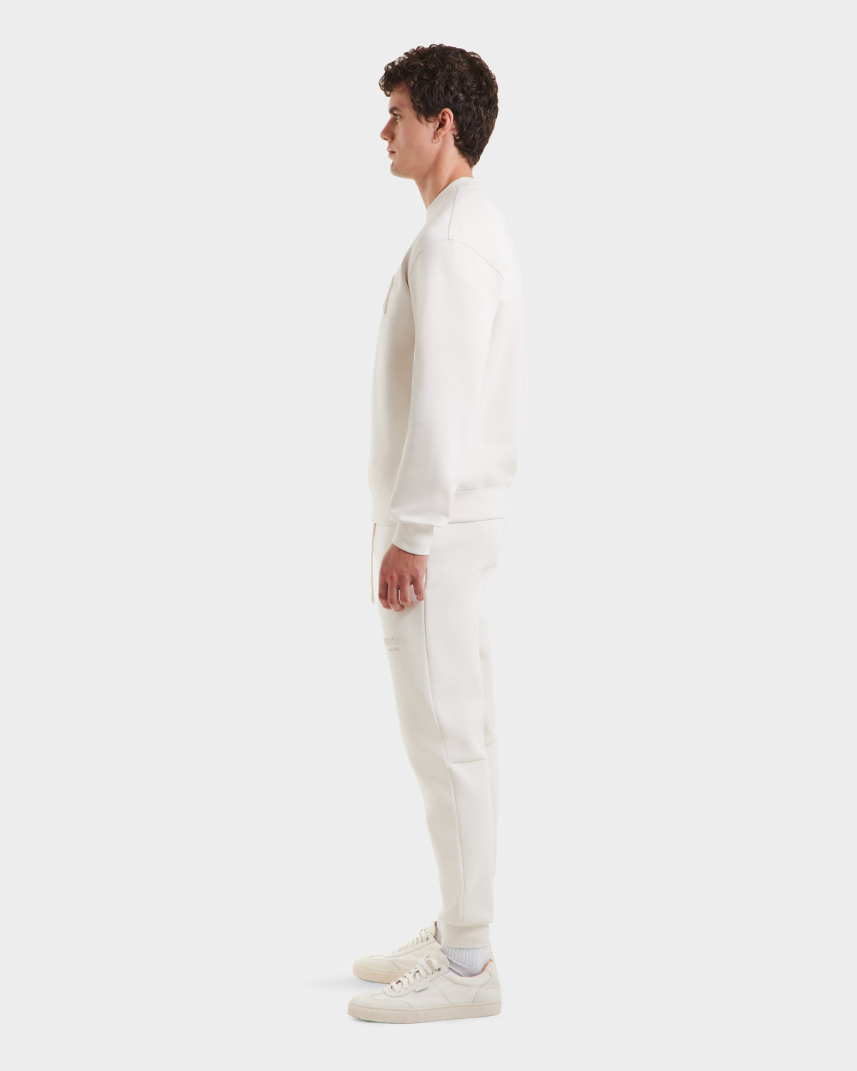 A man stands in profile against a white background, wearing the Rudsak MILOS - 6525646 Vanilla men’s crewneck sweatshirt made from a premium cotton blend. He faces right with arms relaxed at his sides.
